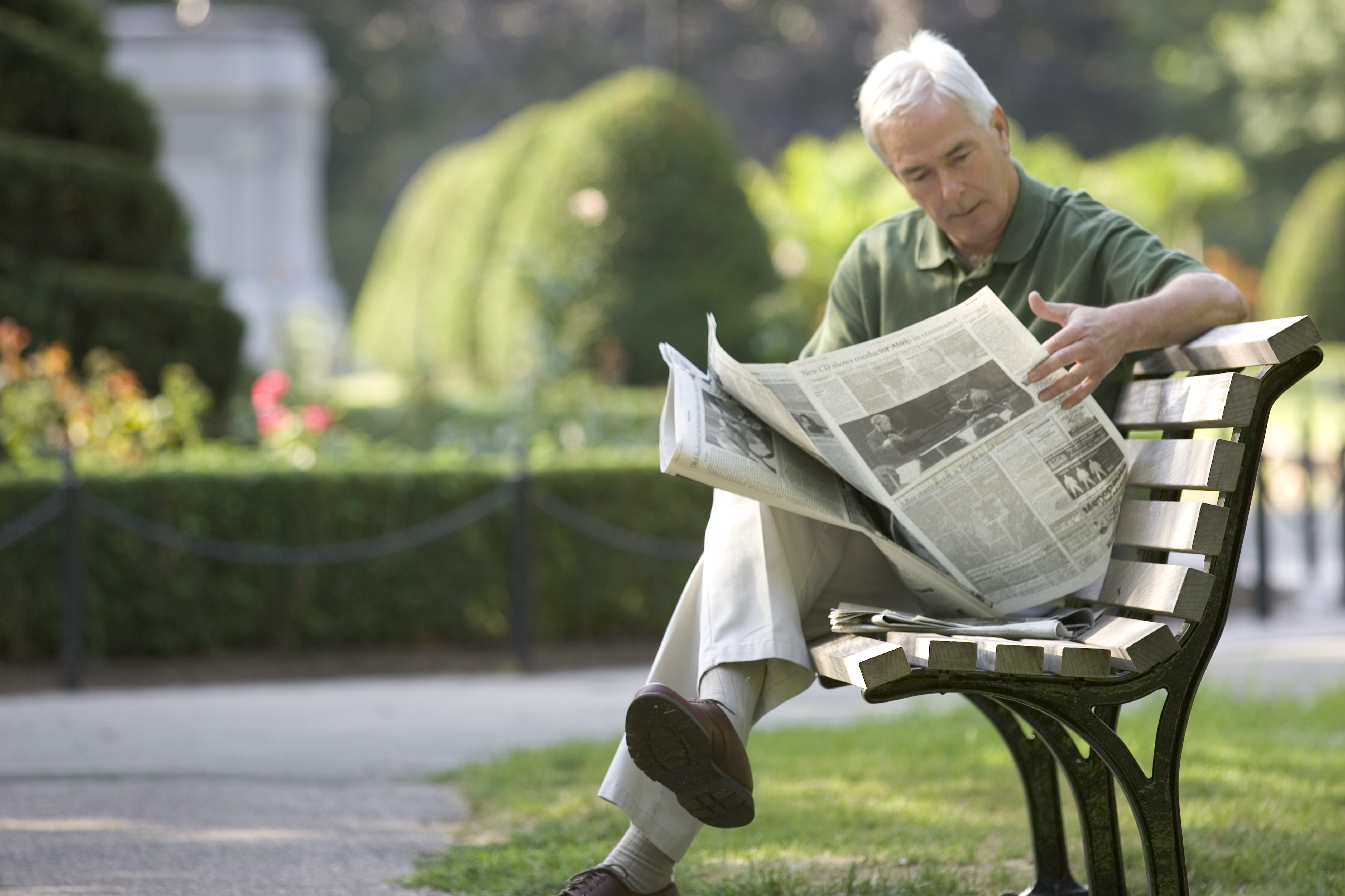 Senior man reading newspaper on park bench, Boston, Massachusetts