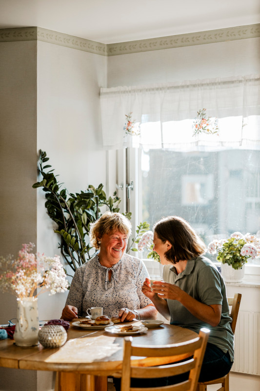 Female nurse having breakfast with smiling elderly woman at home