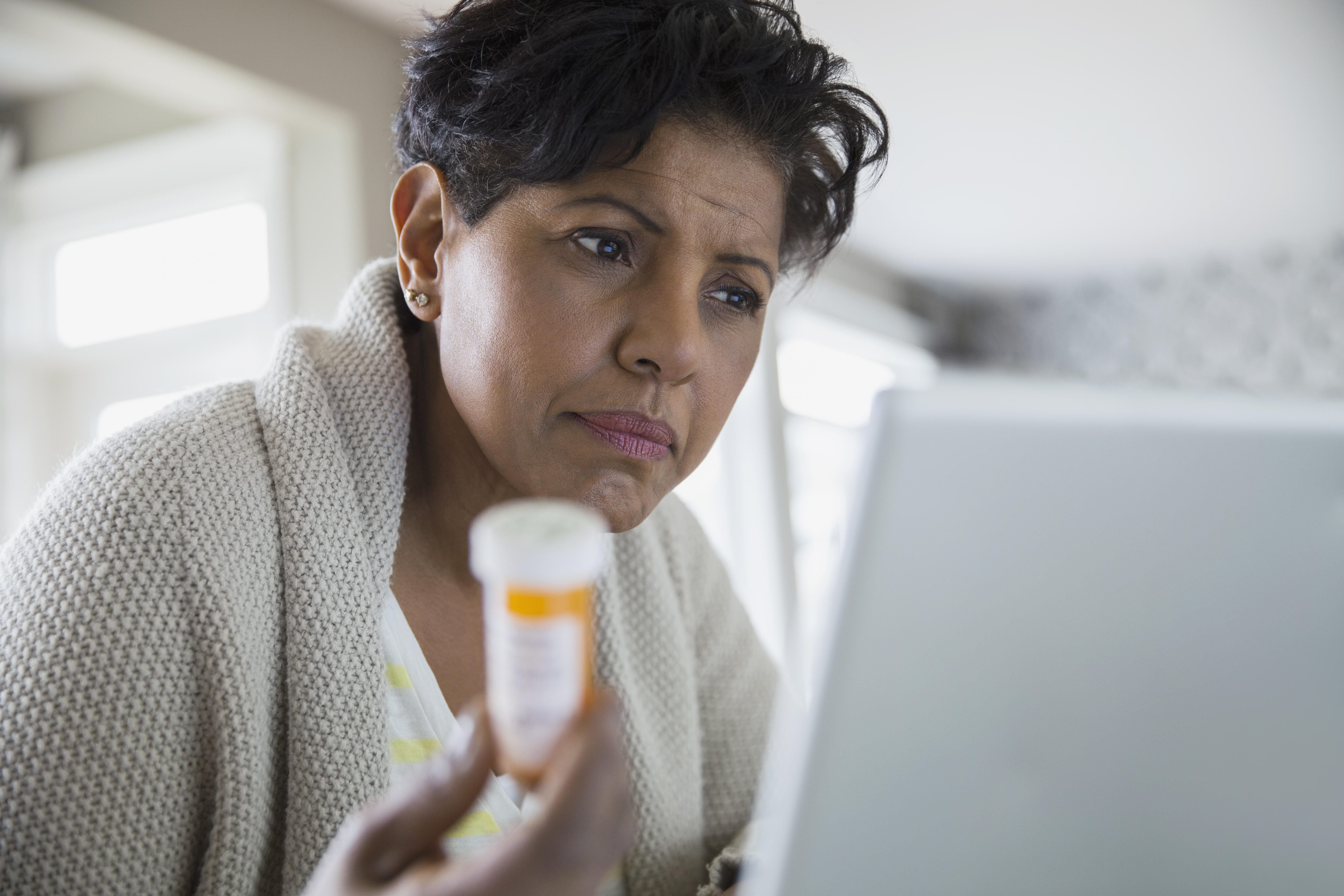 Concerned woman holding prescription bottle at laptop