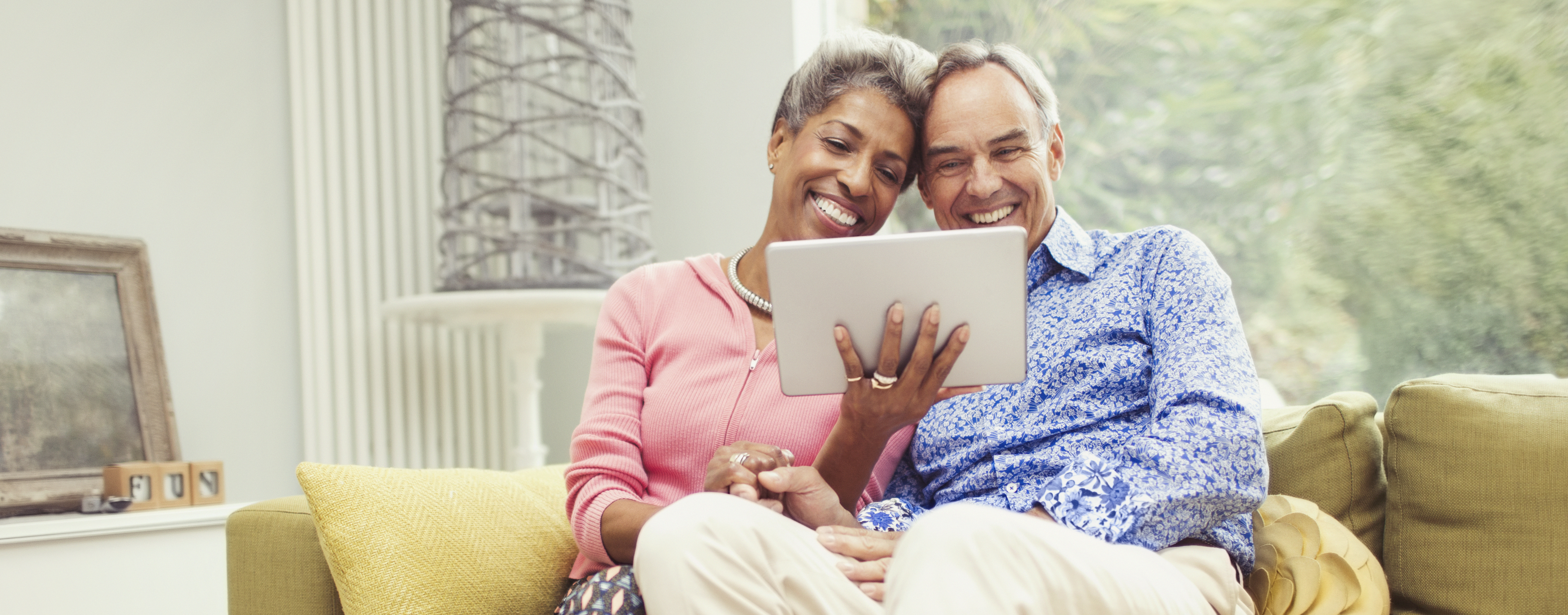 Smiling mature couple using digital tablet on living room sofa