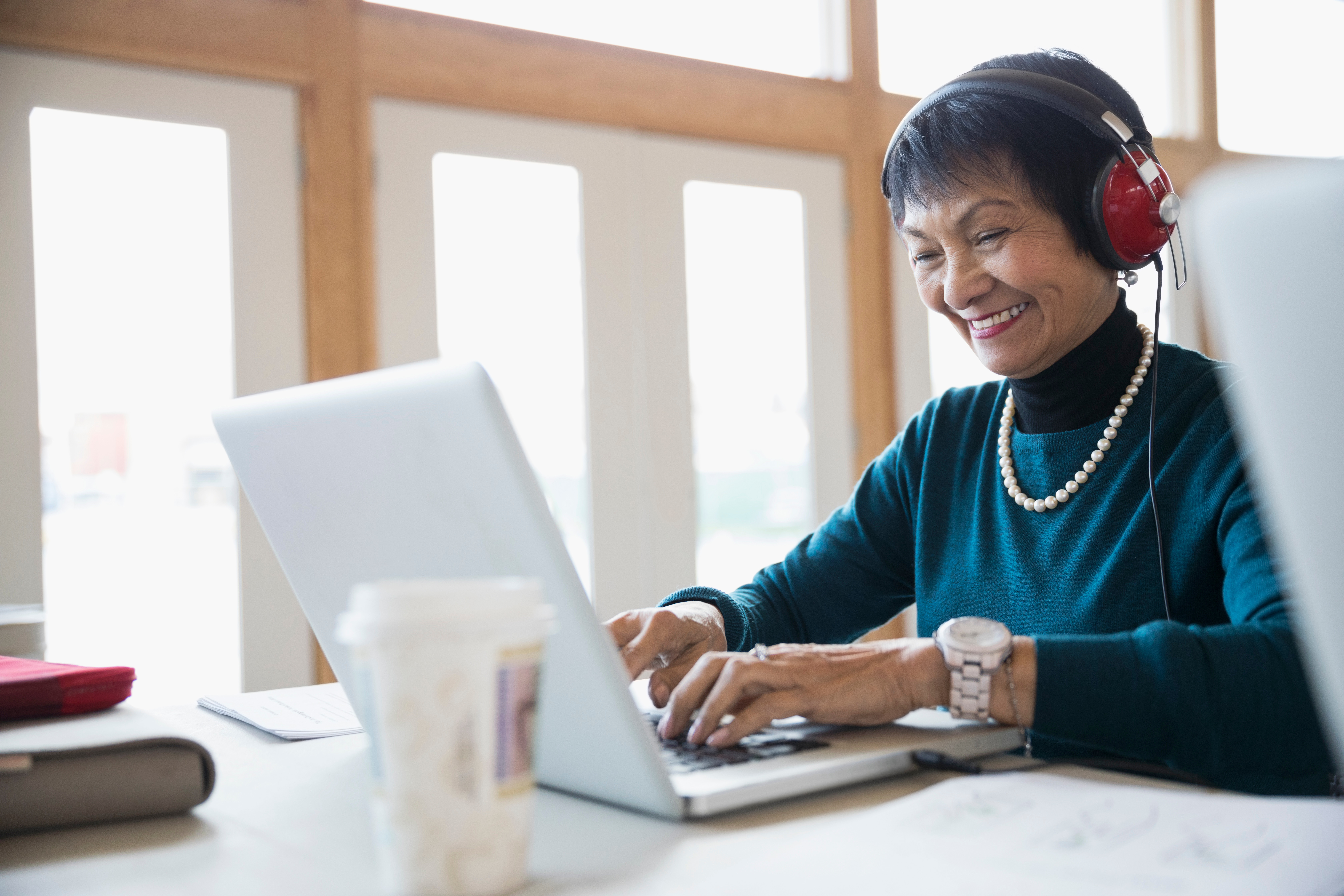 Smiling senior woman student with headphones using laptop in classroom