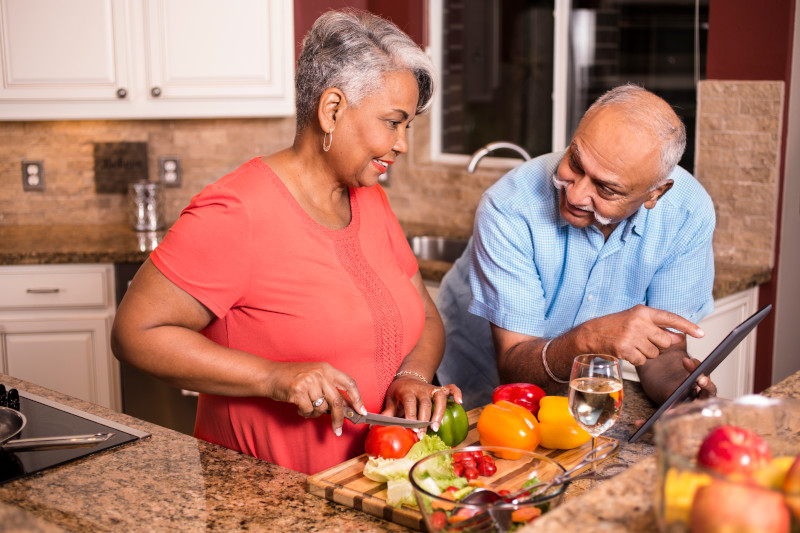 Happy senior adult couple cooking together in home kitchen.