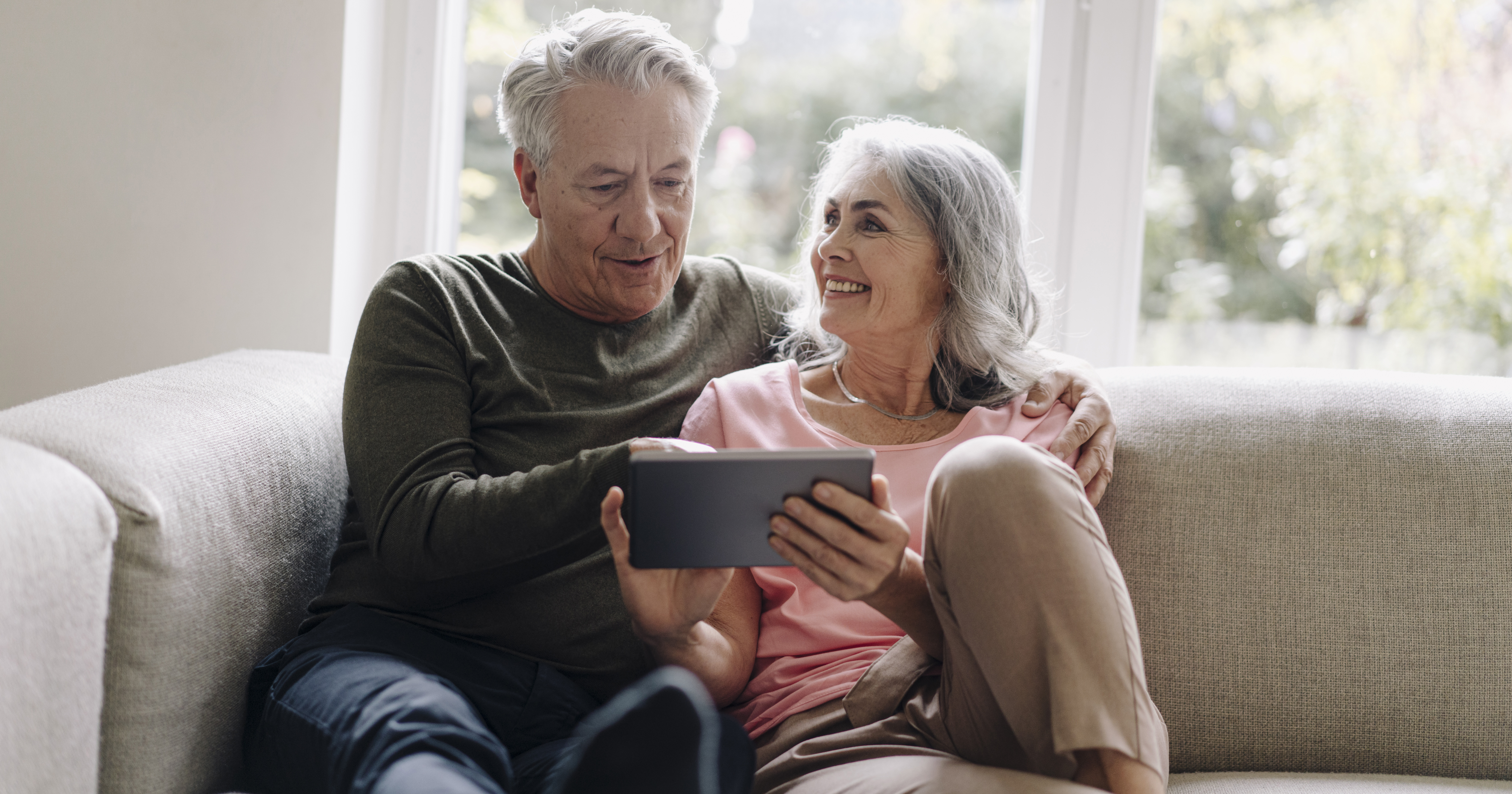 Happy senior couple relaxing on couch at home using tablet