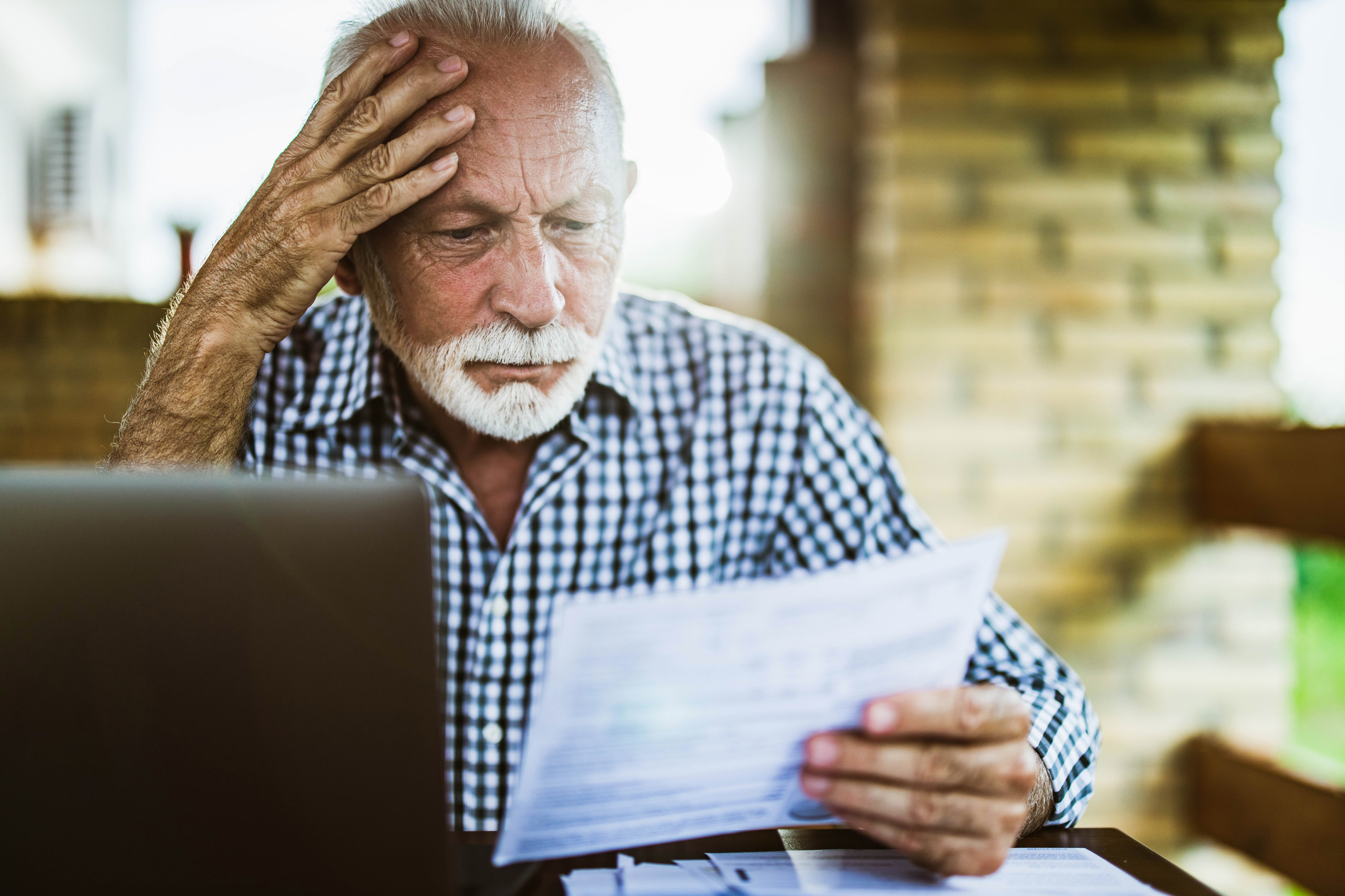 Worried senior man reading his financial bills on a terrace.