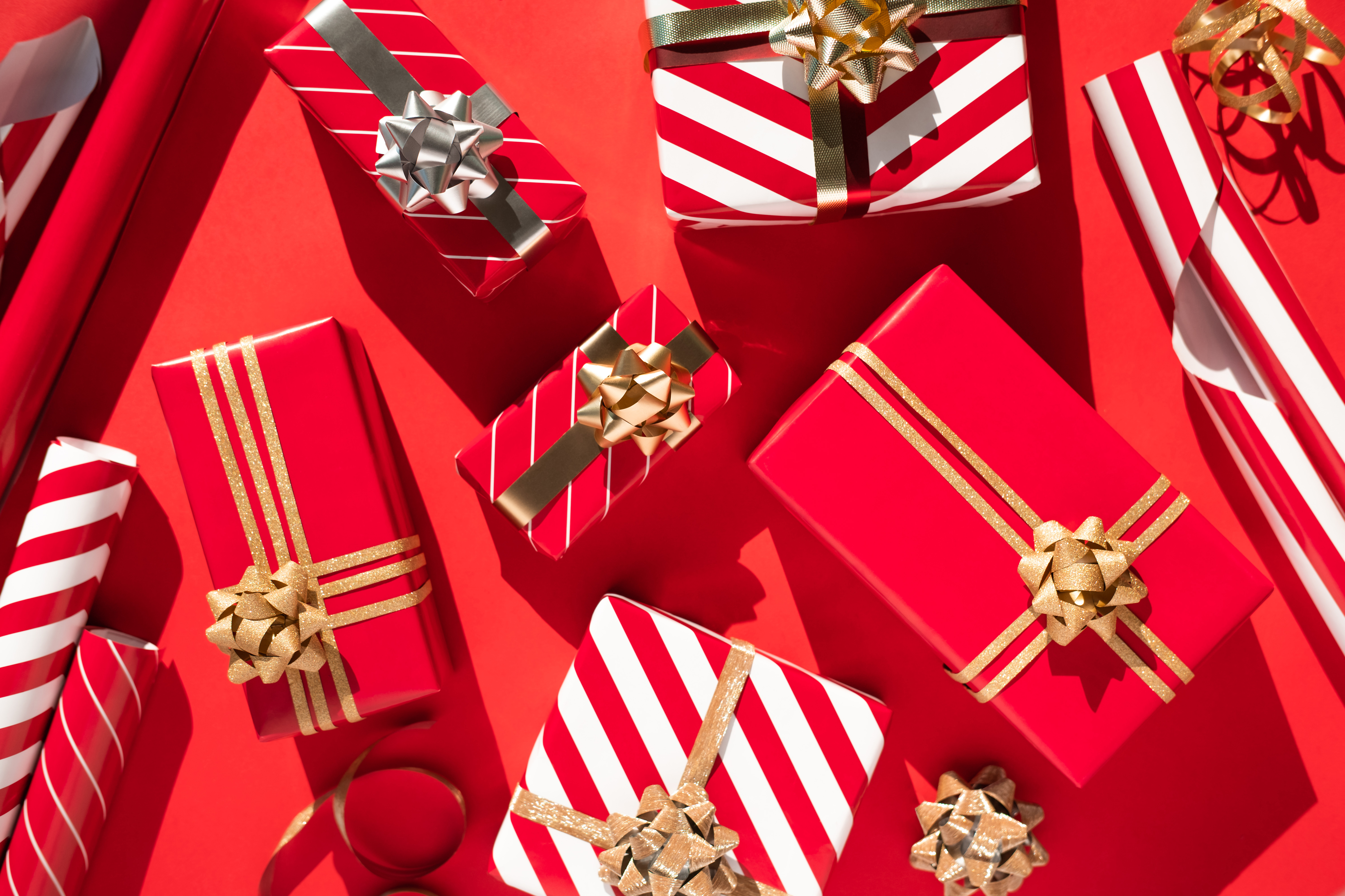 Set of many white-red gift boxes, ribbon, bows and wrapping paper on red table. Flat lay style