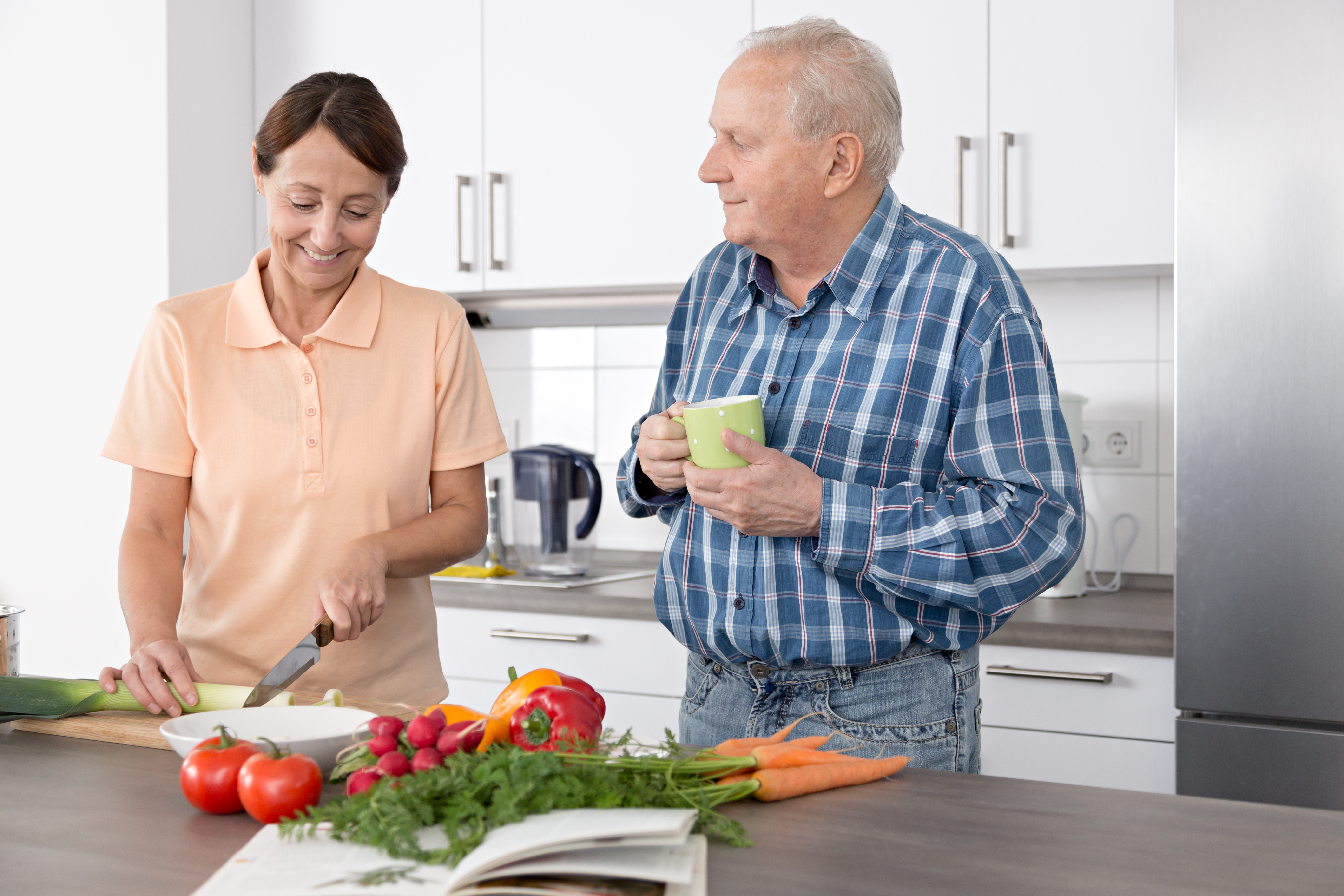 Woman caregiver chopping vegetables with an older man in a kitchen