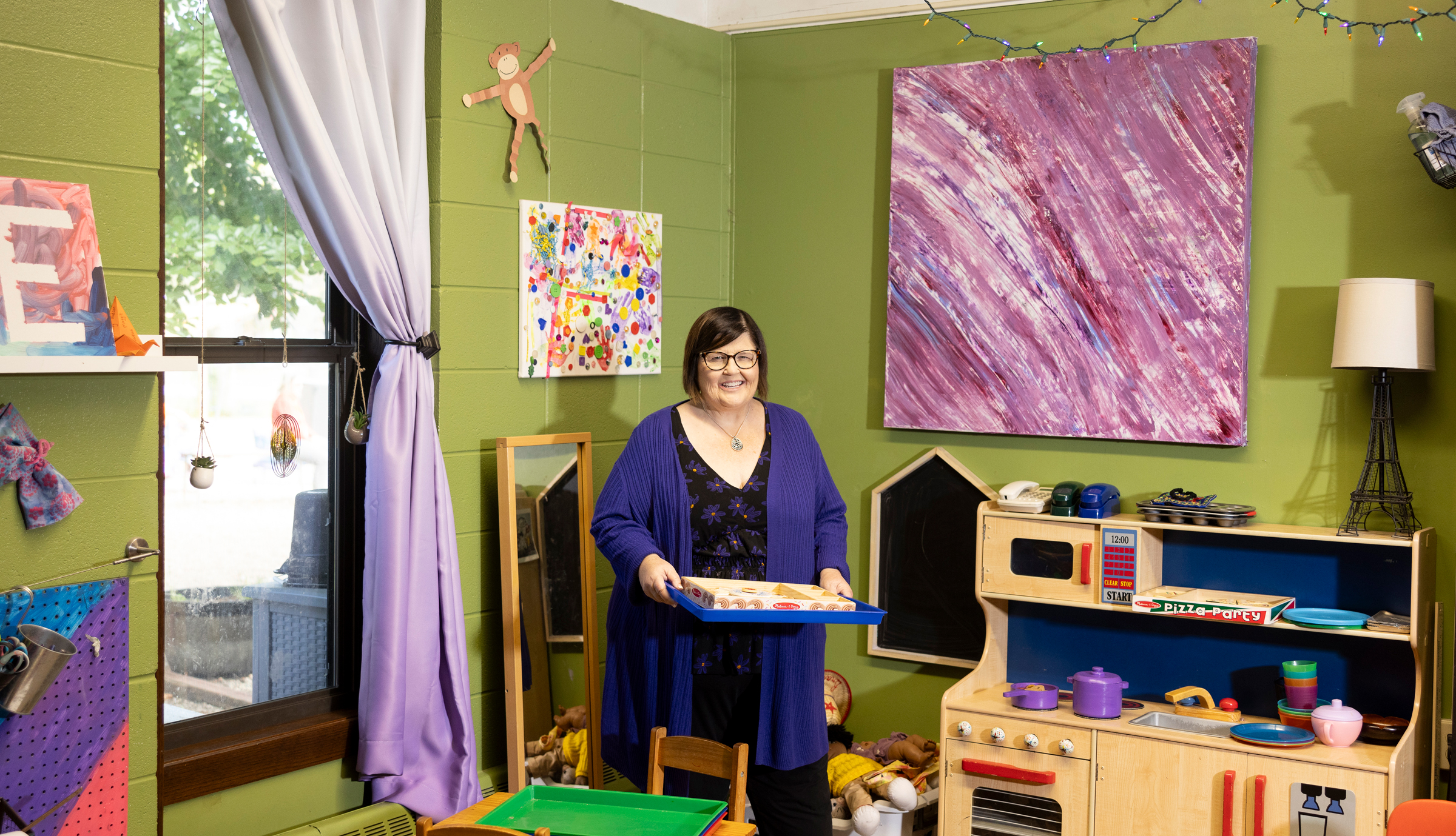 A woman standing in a child care classroom holding a tray