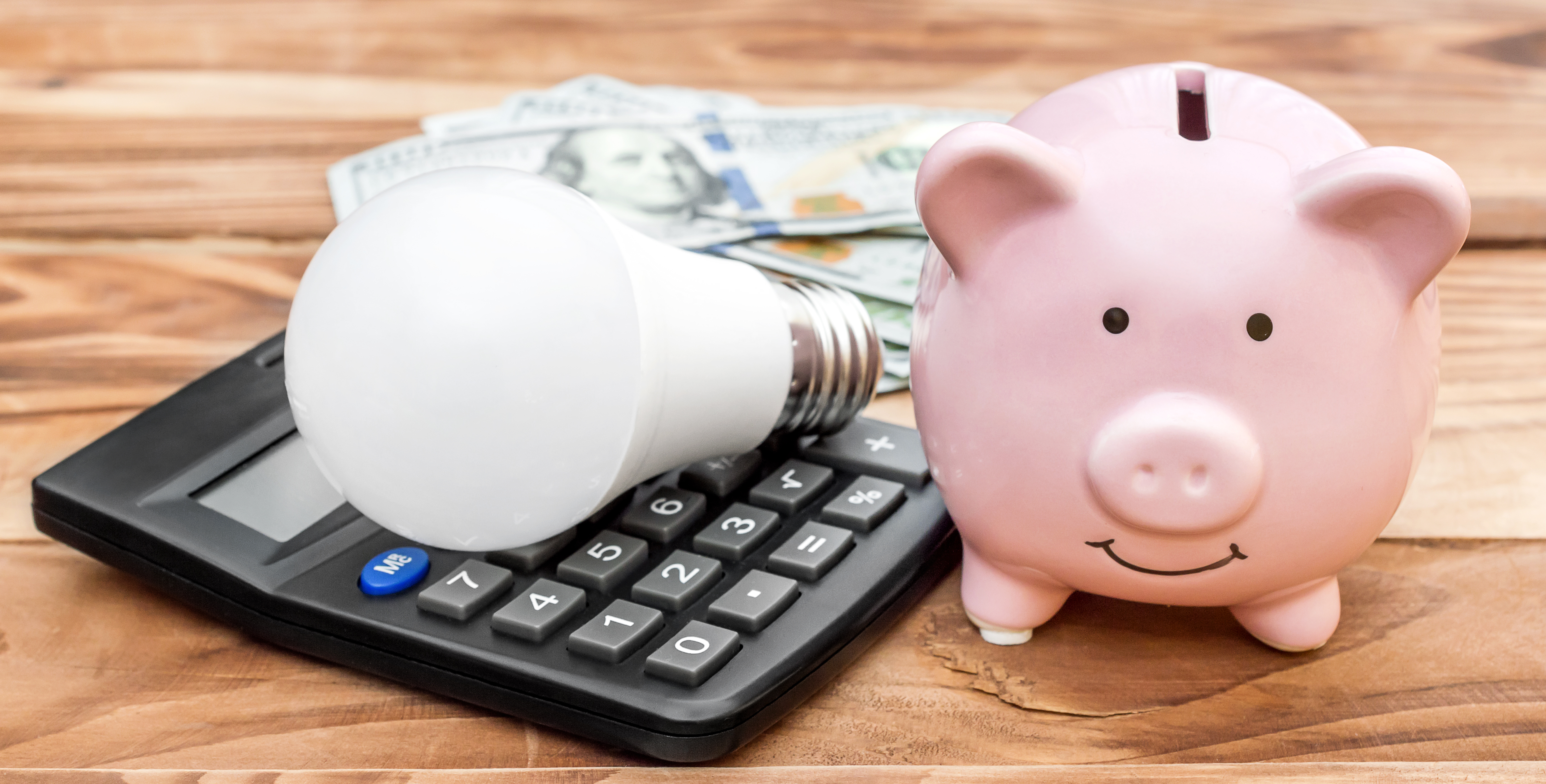 Piggy bank with light bulb, calculator and money on wooden background.