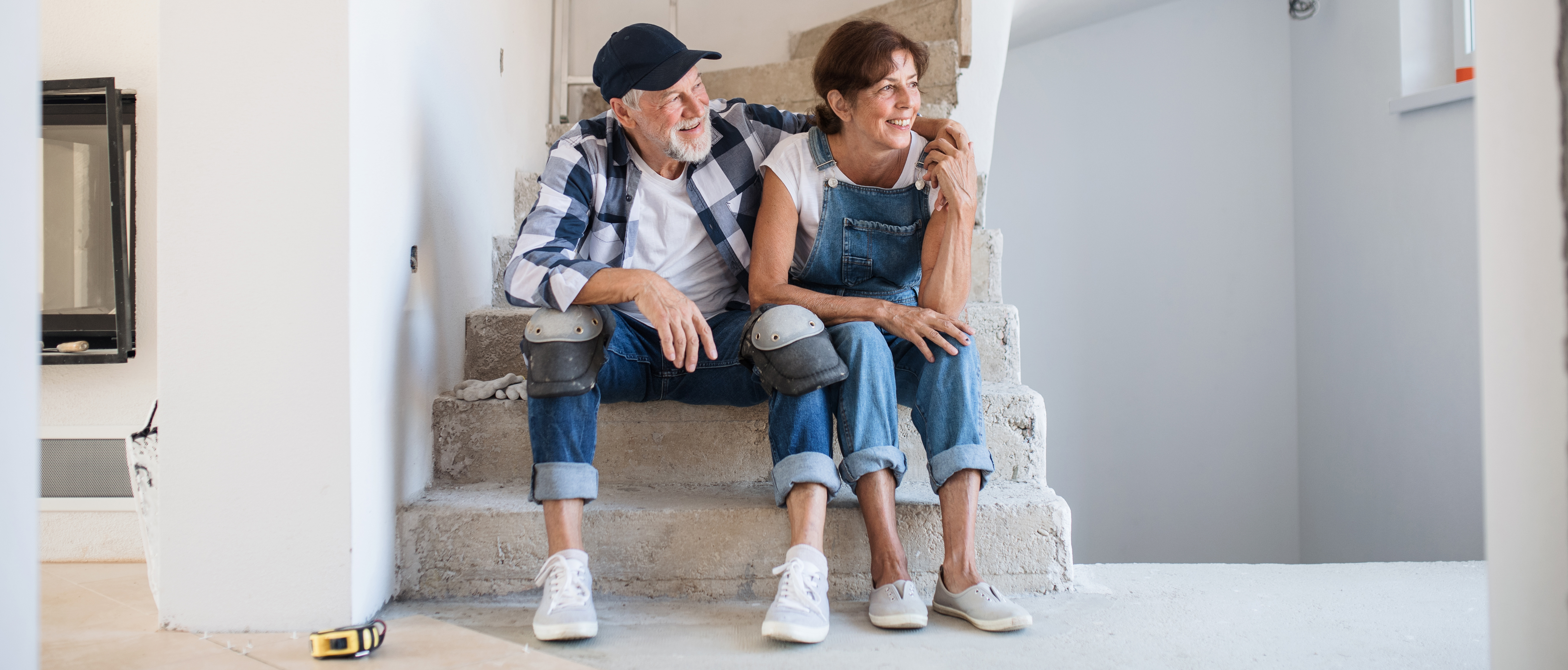 Senior couple laying tile floor in new home, sitting and resting.