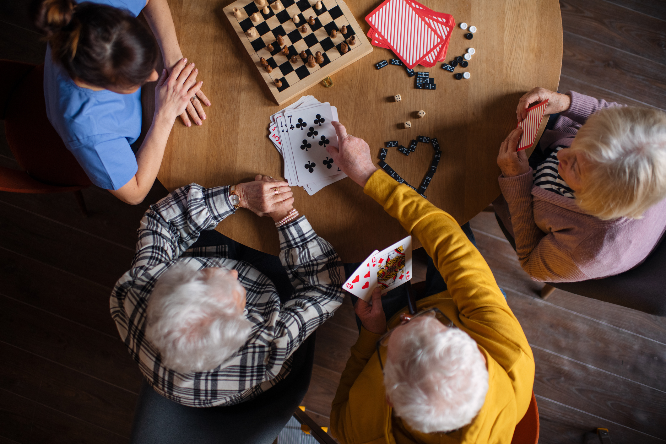 Top view of seniors playing a board game in their retirement home, nurse is playing with them.