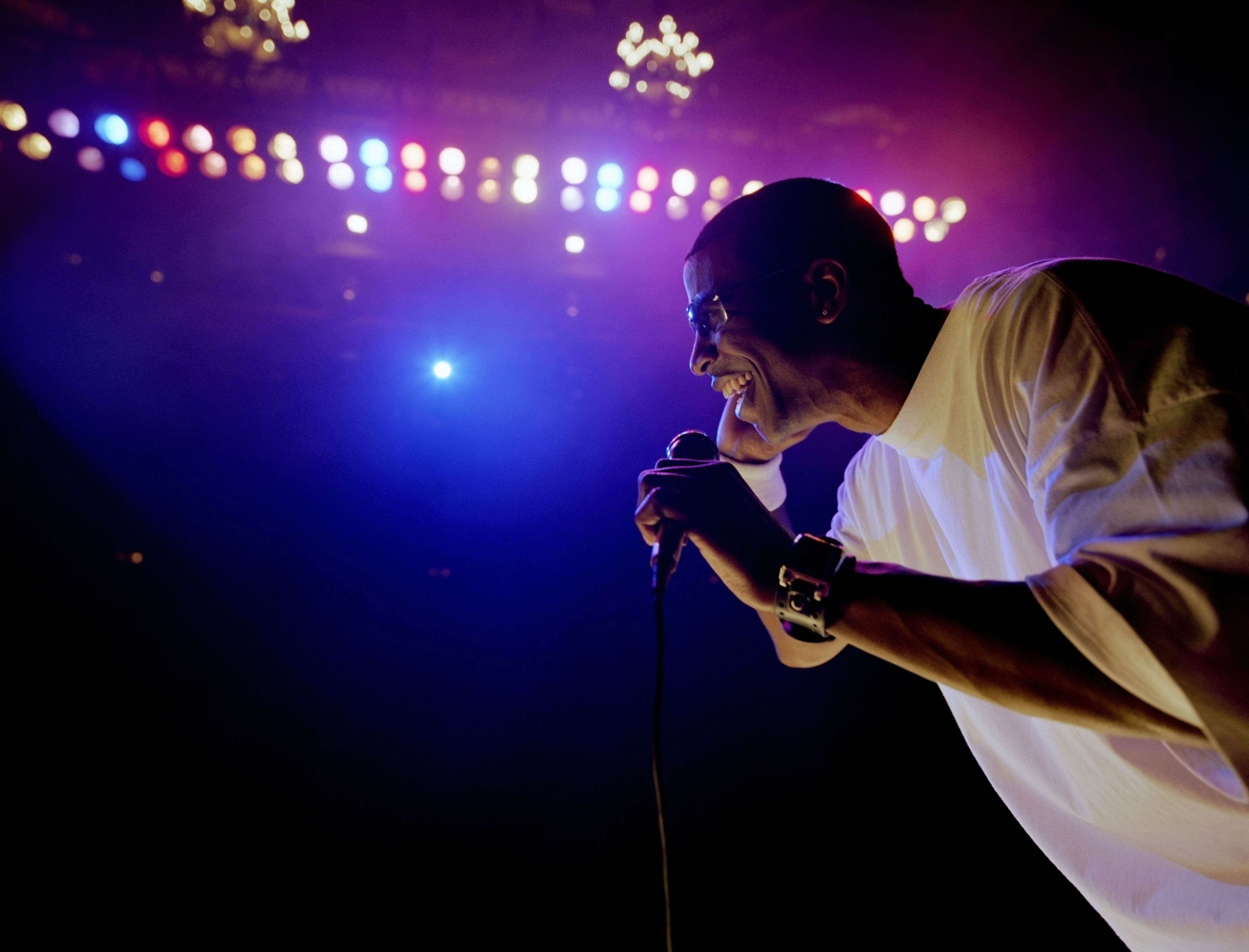 Comedian standing on stage, holding microphone, profile