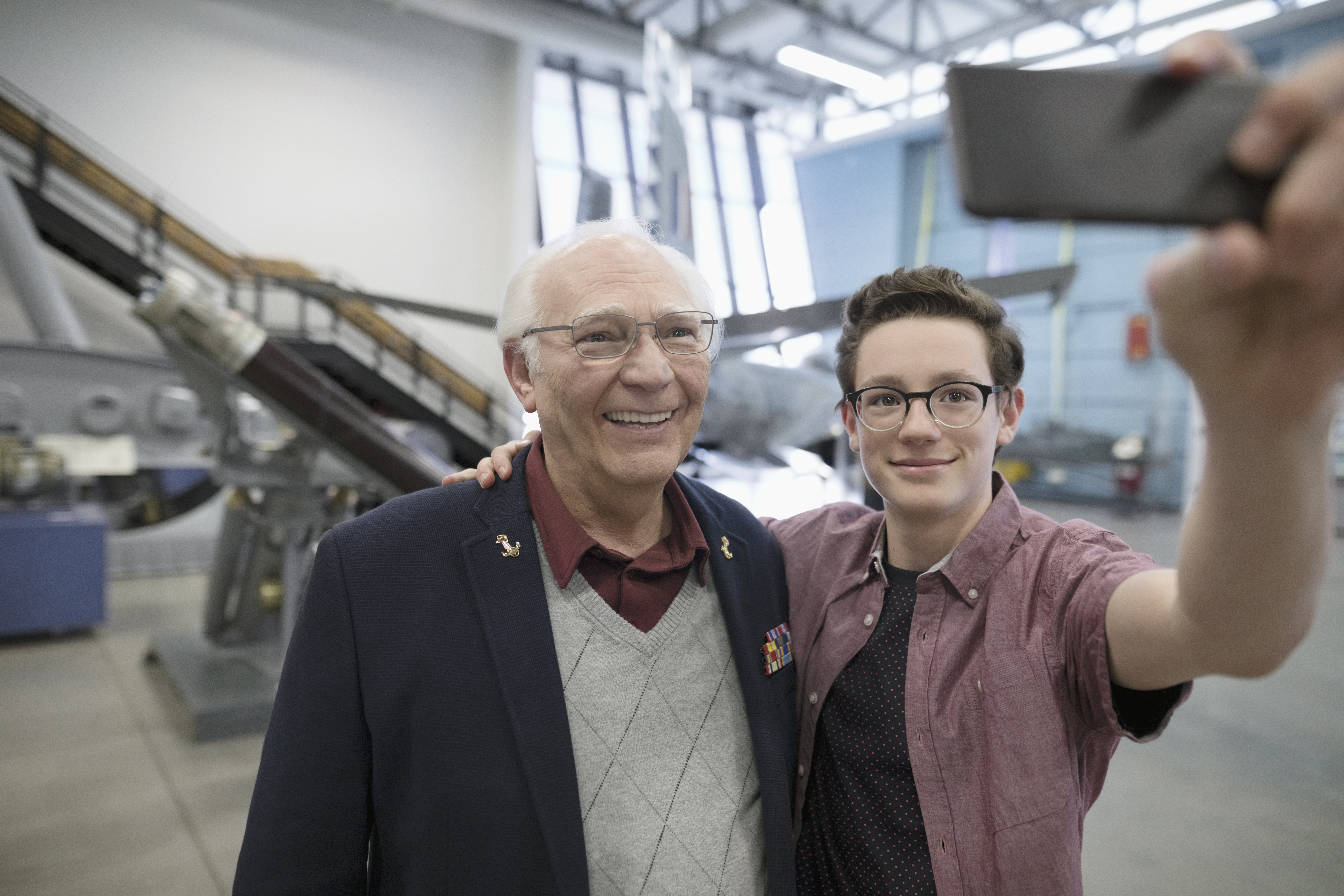 Grandfather and grandson with camera phone taking selfie in war museum hangar