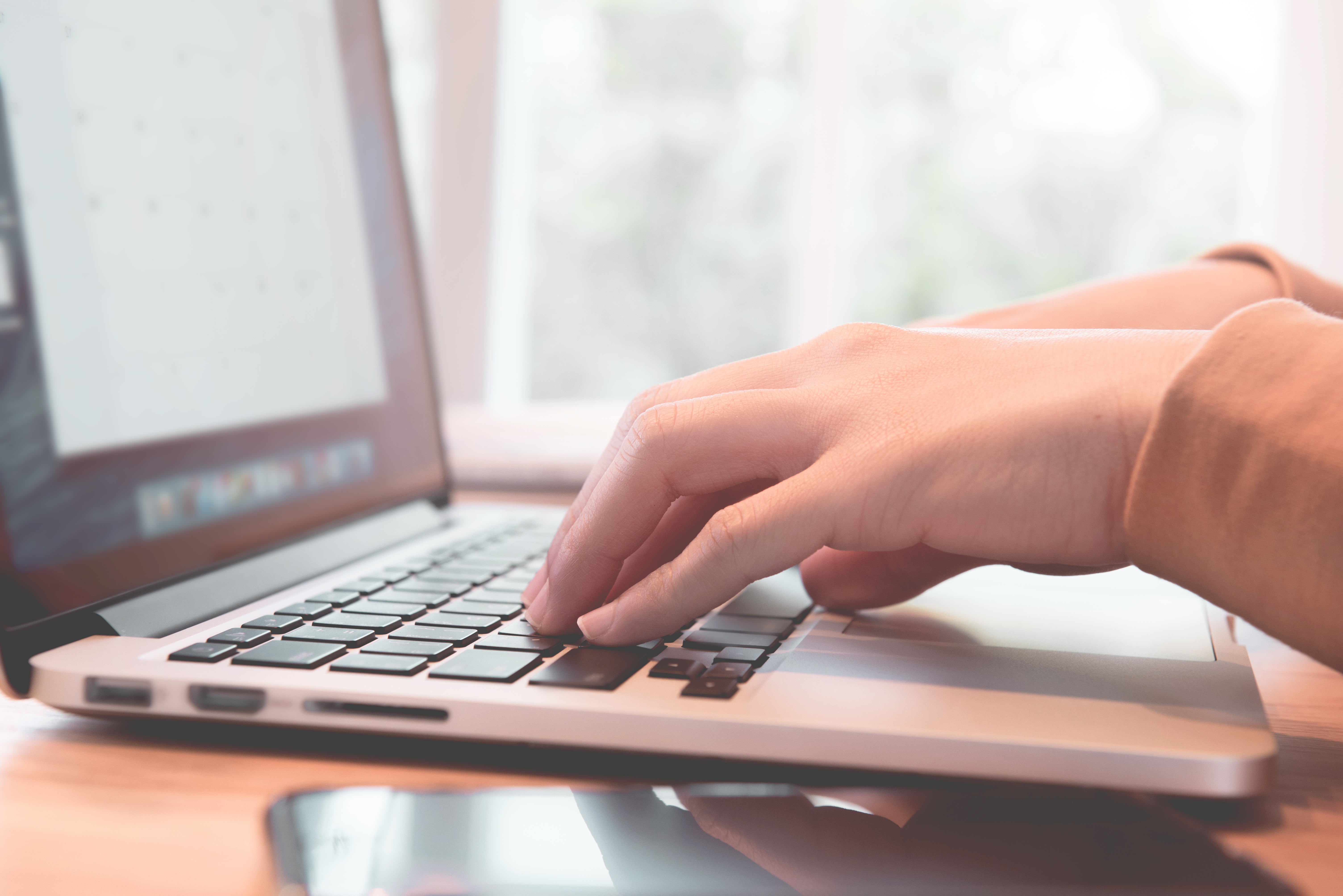 Closeup woman's hands using on a laptop on a wooden desk