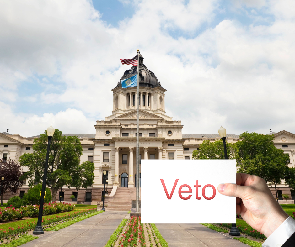 Picture of the SD Capitol with a man's hand holding a sign in front that says Veto.