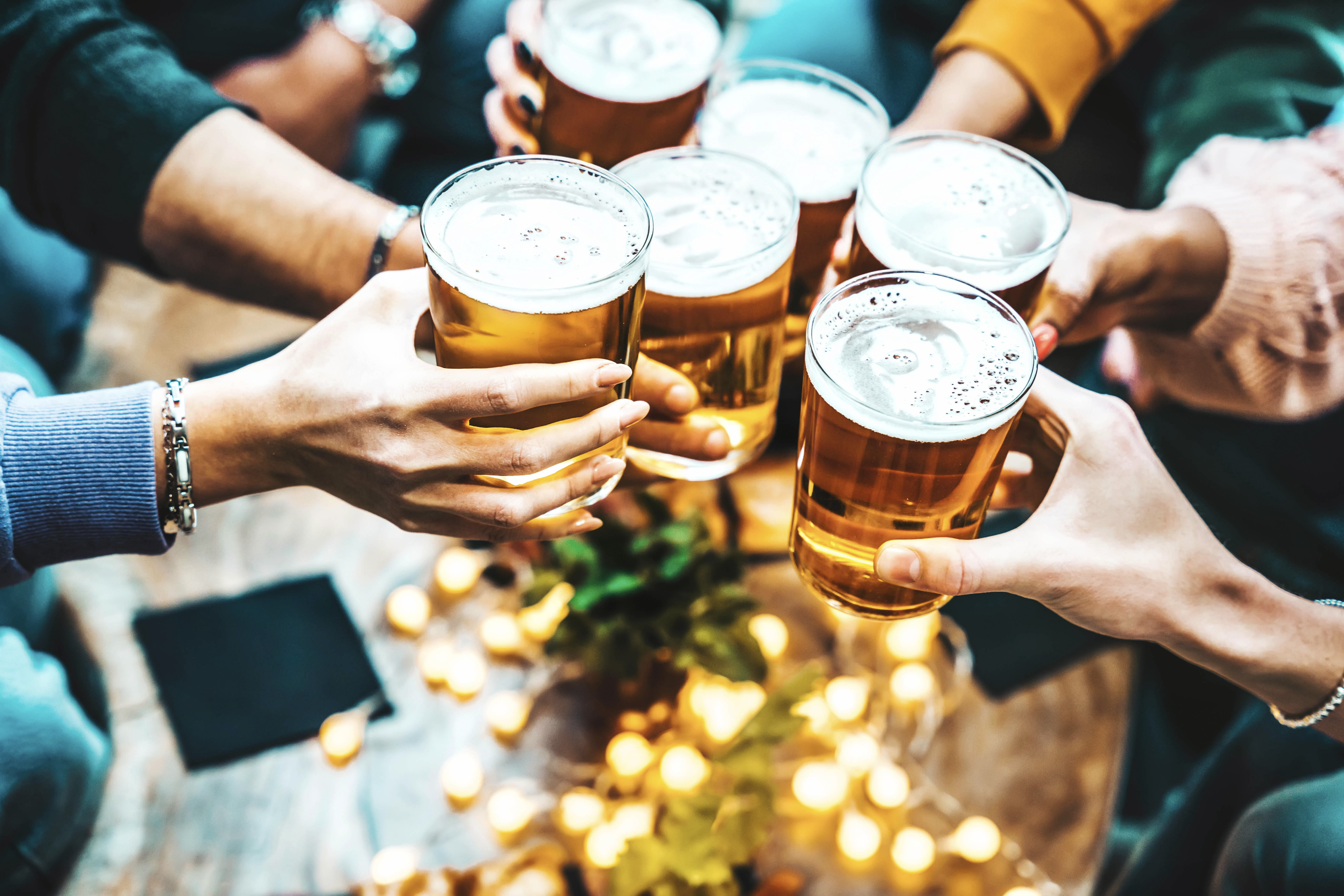 Group of people drinking beer at brewery pub restaurant - Happy friends enjoying happy hour sitting at bar table - Closeup image of brew glasses - Food and beverage lifestyle concept
