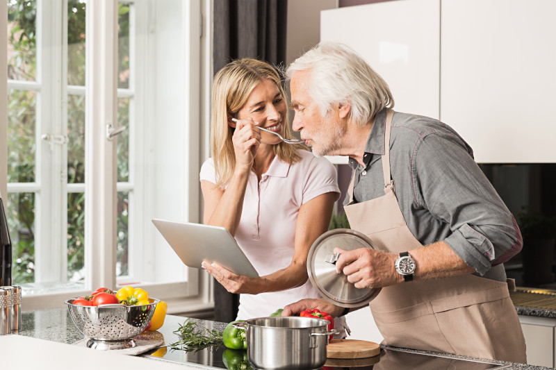 Senior man cooking with daughter, tasting food