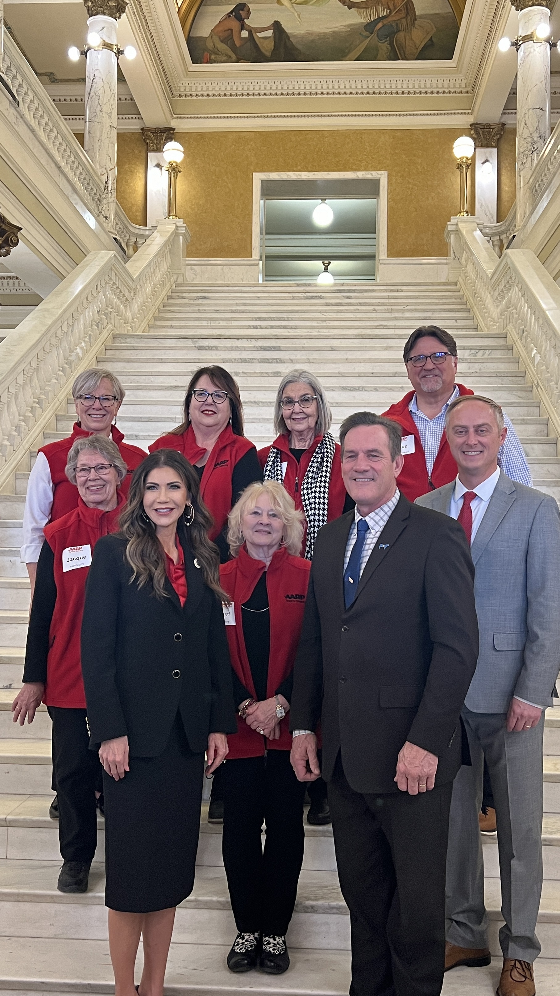 South Dakota Governor and Lieutenant Governor with seven representatives from AARP South Dakota standing on the Capitol Rotunda steps in Pierre.