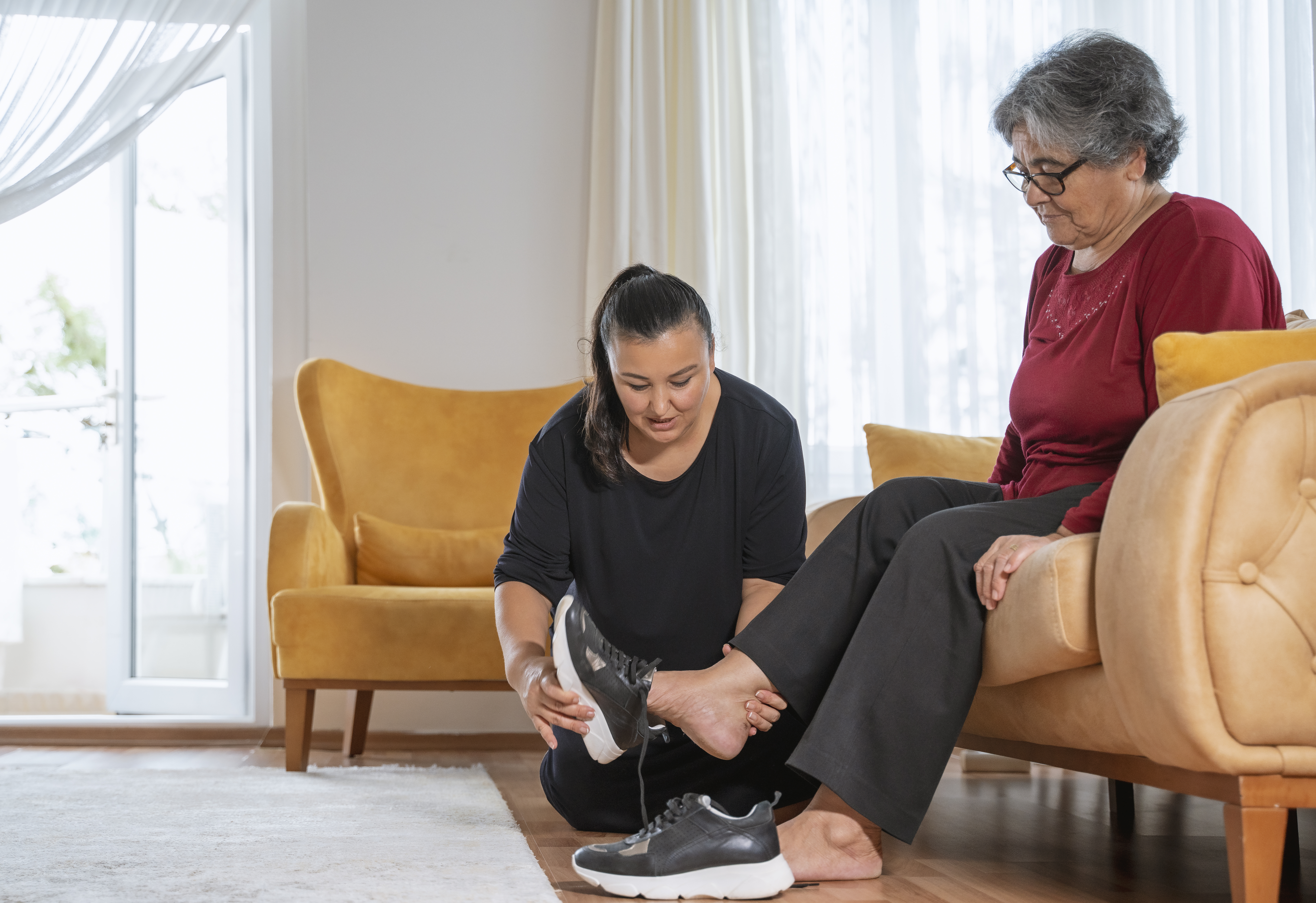 Woman helping her elderly mother in wearing shoes at home