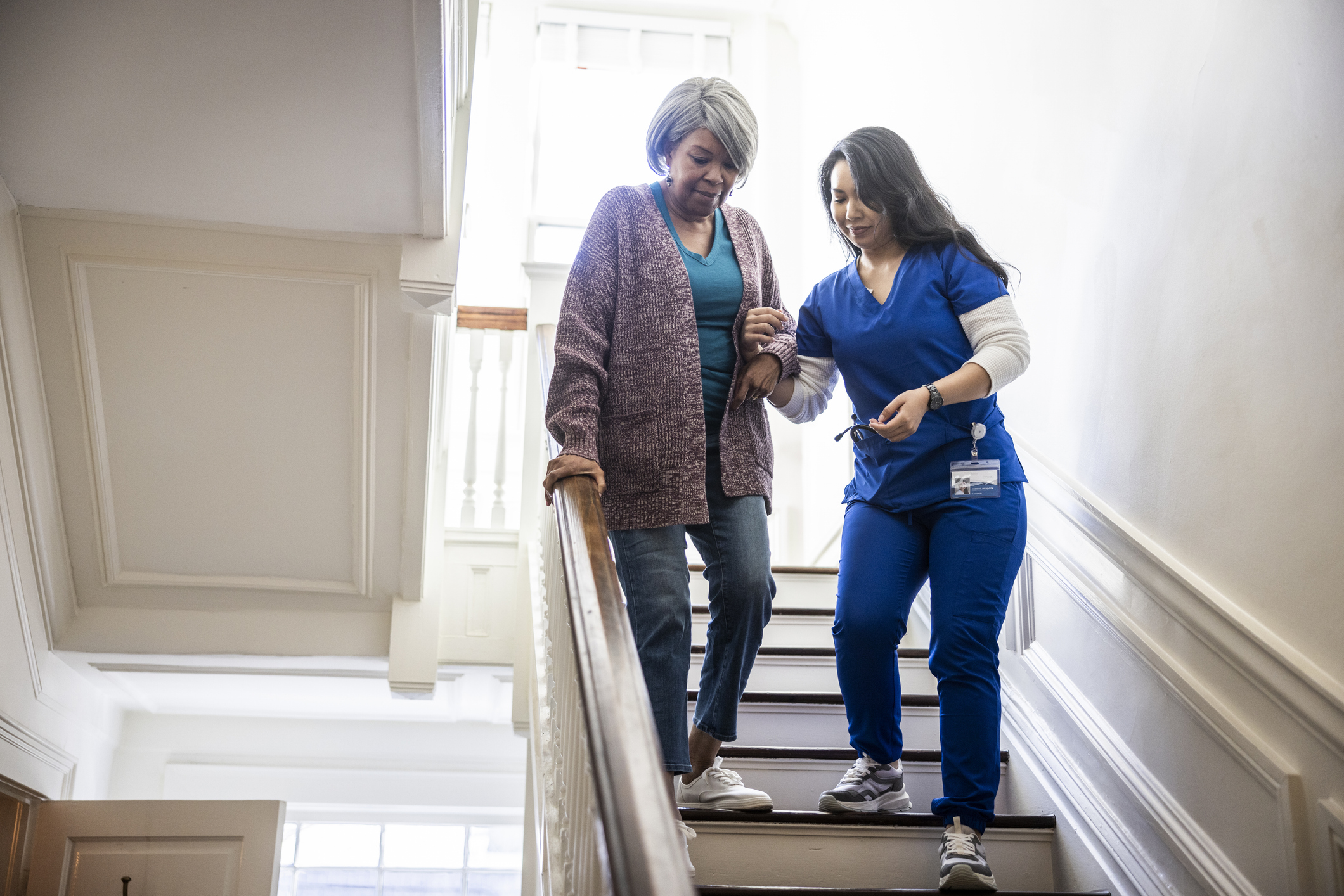 In-home nurse helping senior woman down a staircase