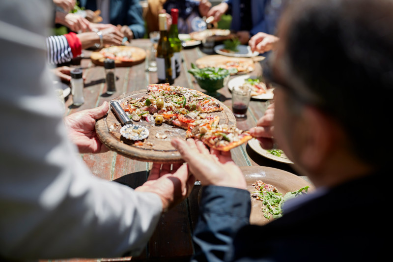 Friends sharing homemade pizza at sunny patio table