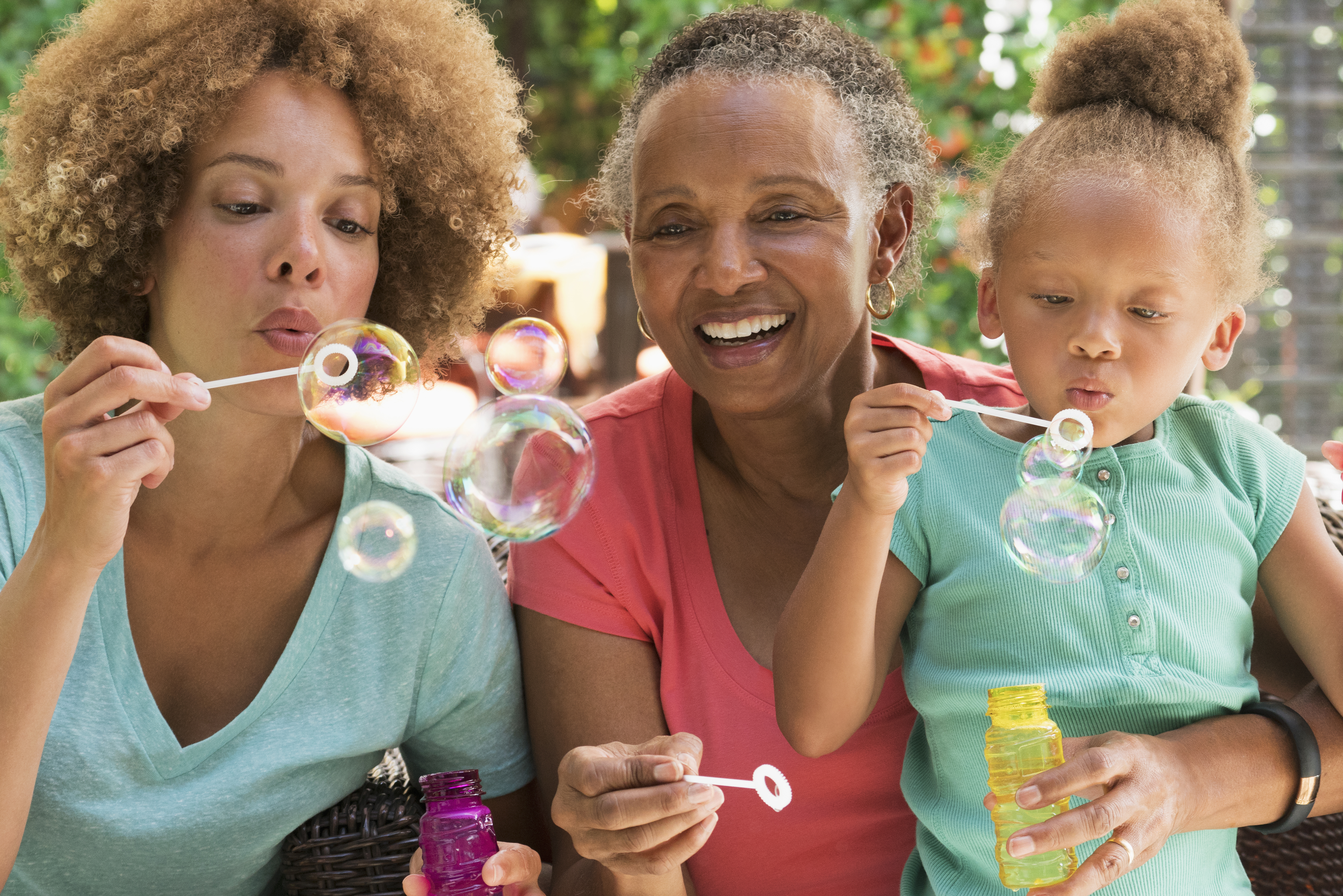 Black multi-generation family blowing bubbles outdoors