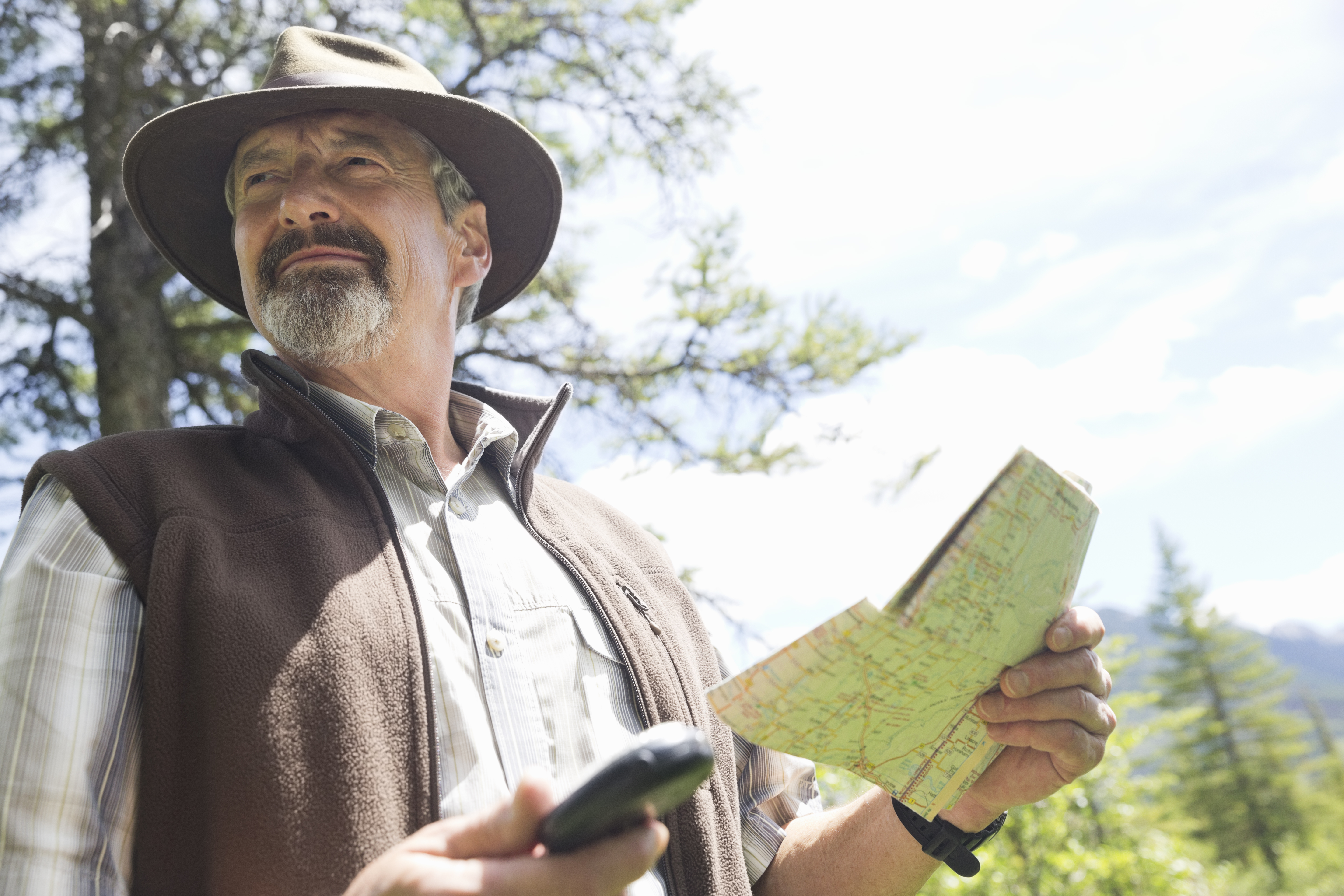 Senior man holding map and compass in forest