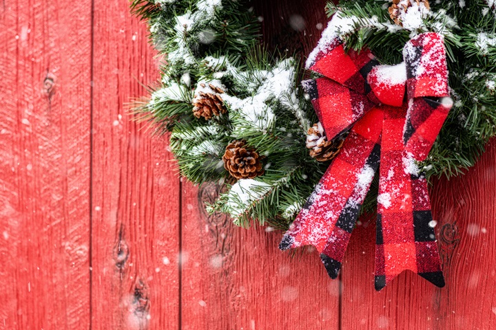 Christmas wreath with plaid bow on red barn while it snows