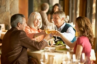 Four mature adults toasting with white wine in restaurant, smiling