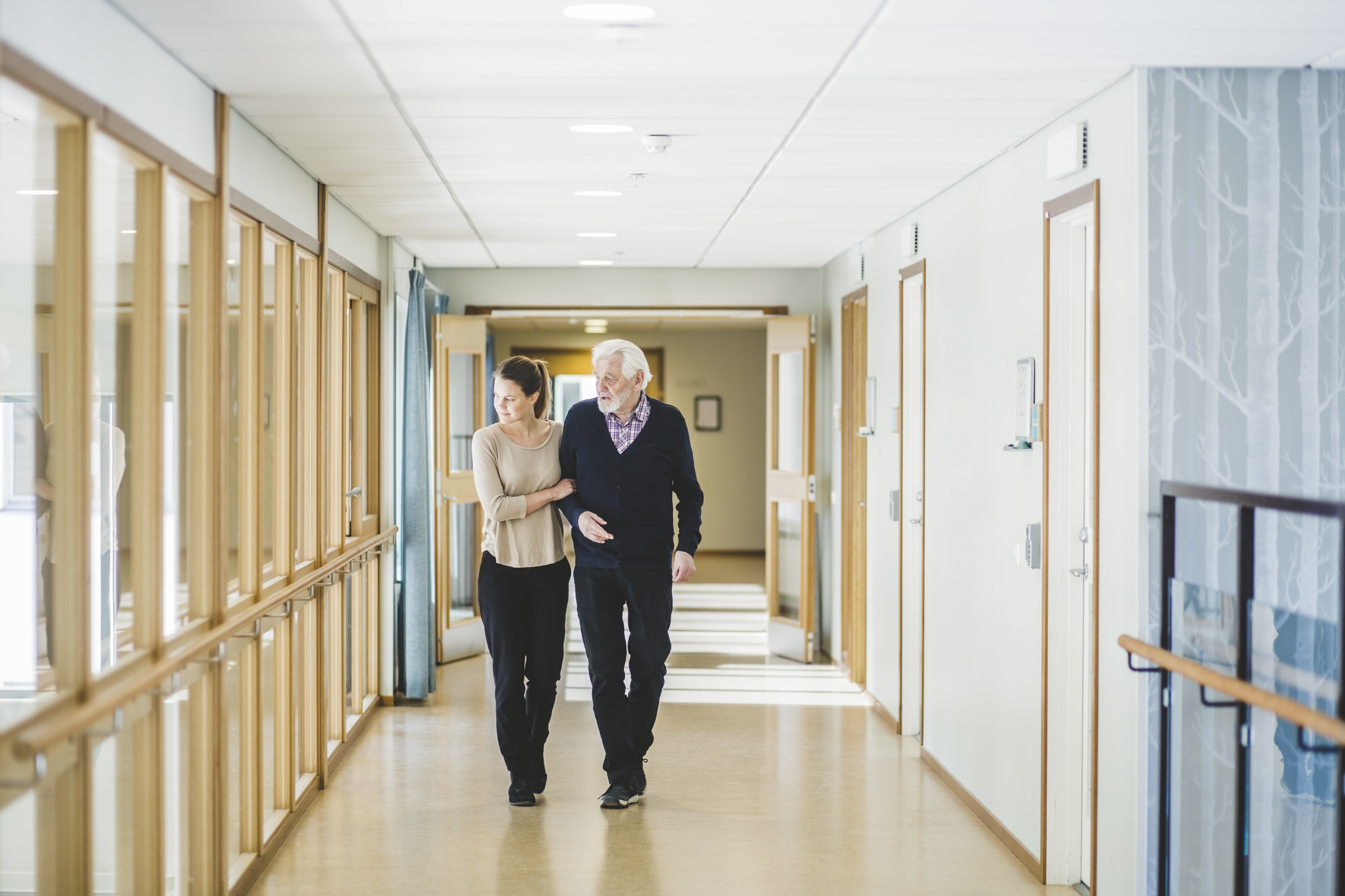 Young woman looking away while walking with grandfather in corridor at nursing home