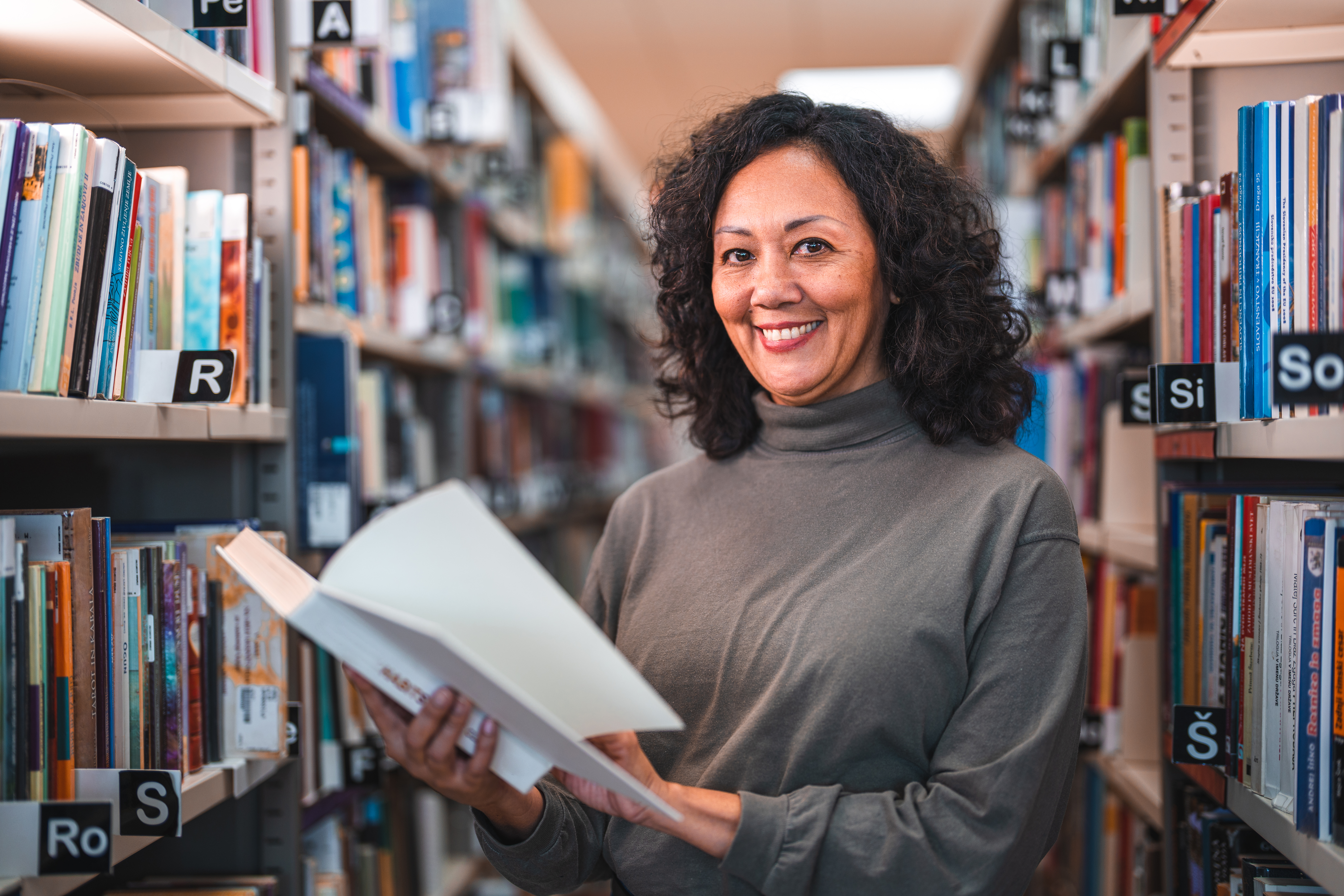 Latin Female in 60s Reading A Book In A Library