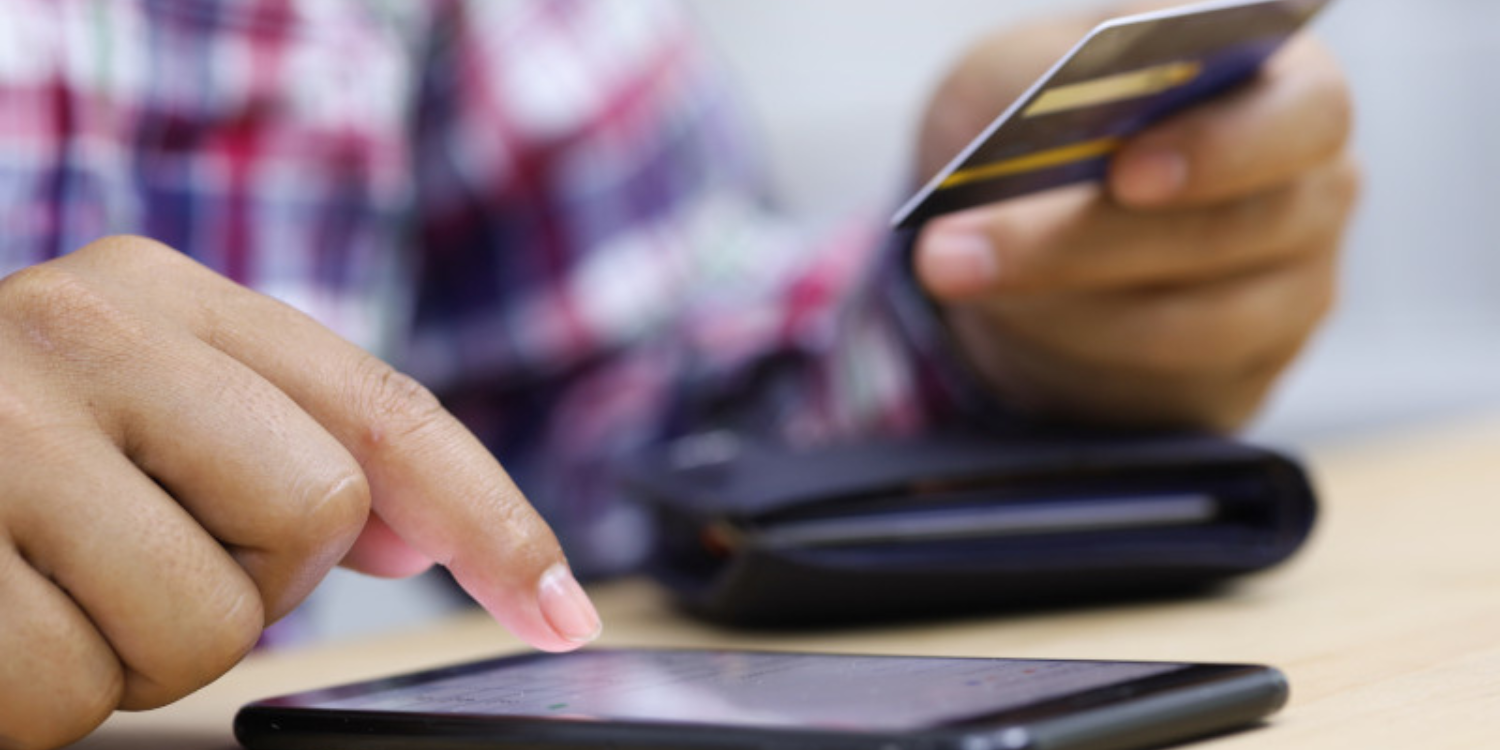 A person holds a credit card and types in information into a mobile phone.