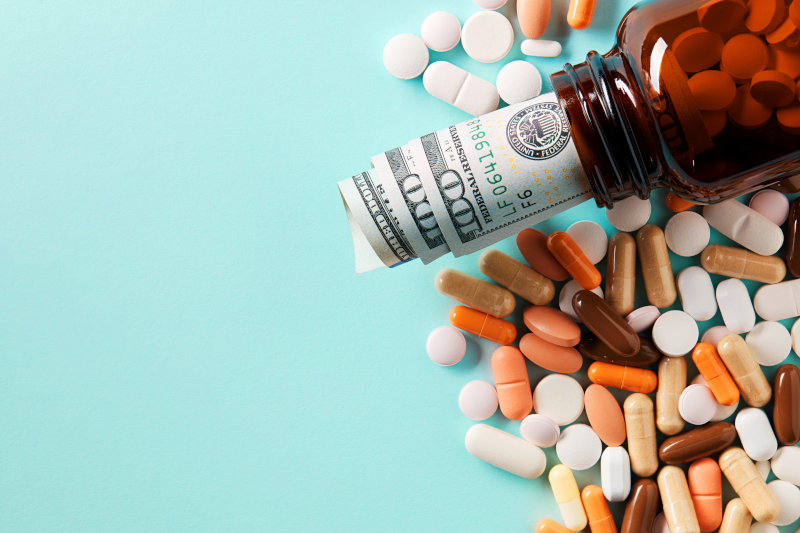 A medicine bottle stuffed with money atop a variety of pills.