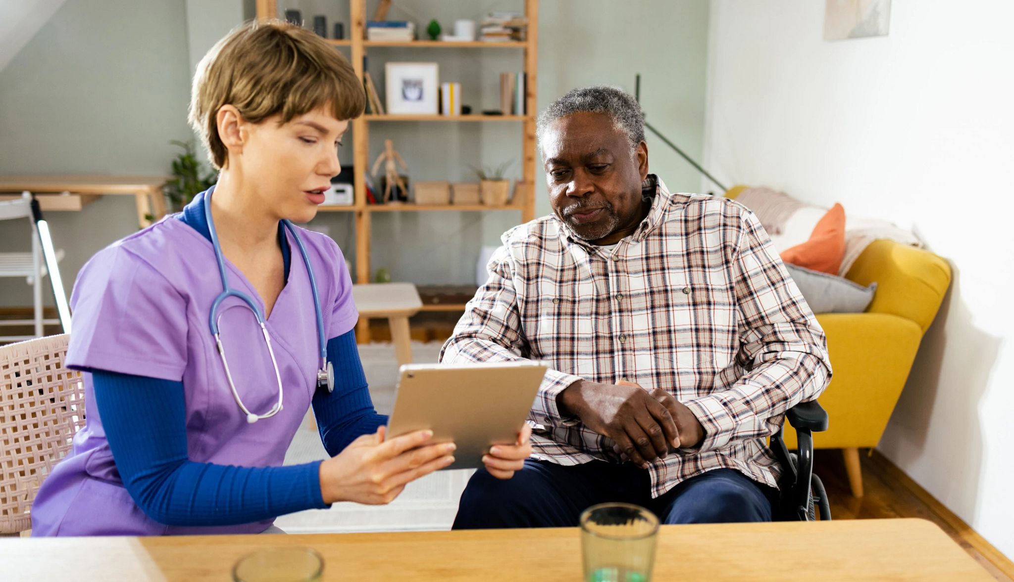 Young healthcare worker or caregiver visiting senior woman indoors at home, talking and writing.