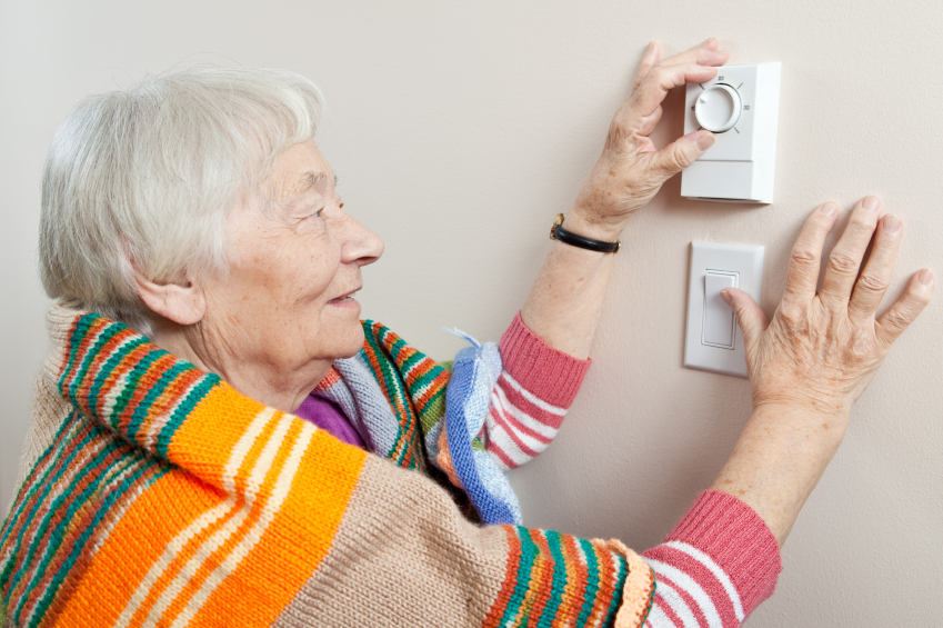 Elderly woman adjusting thermostat for heat