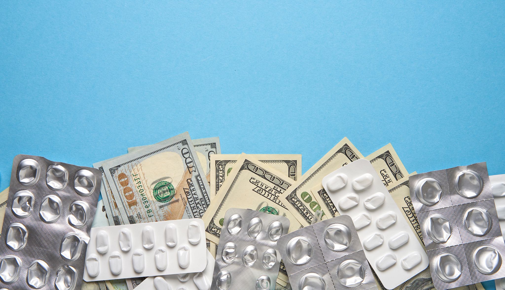 empty blister packs for prescription drugs and various dollar bills lie on a blue background
