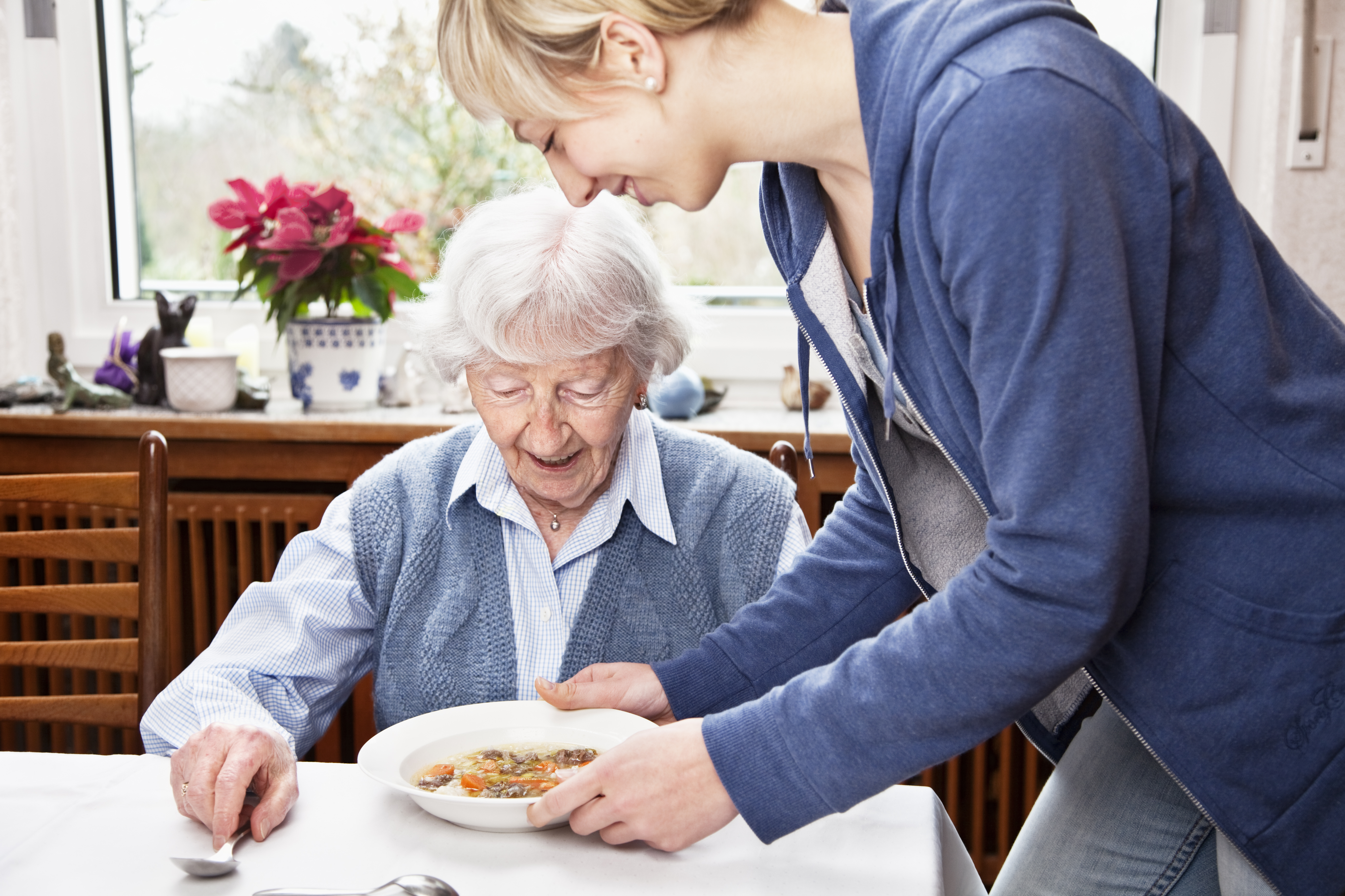 senior woman getting soup served by caregiver