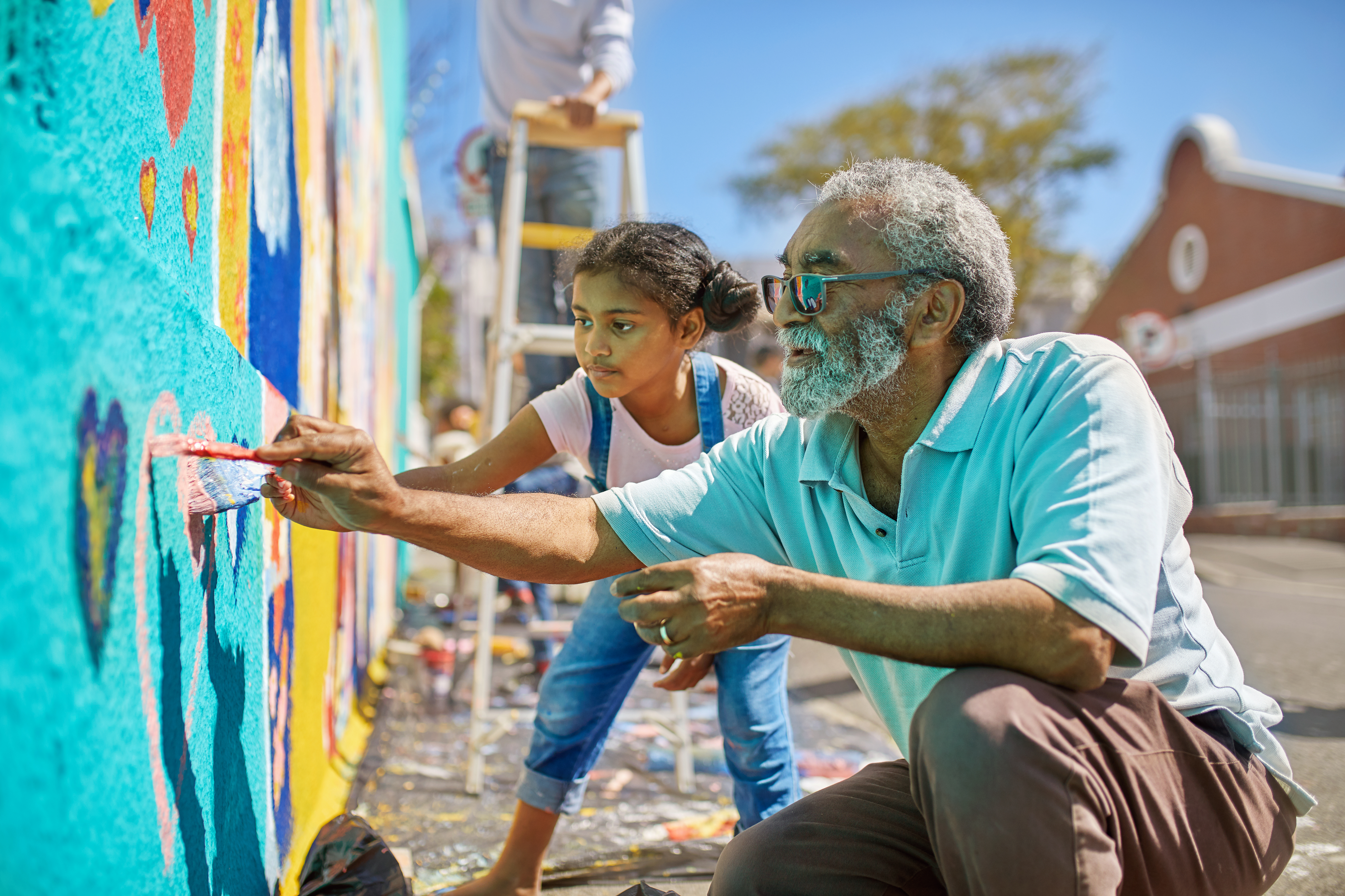 Grandfather and granddaughter volunteers painting vibrant mural on sunny urban wall