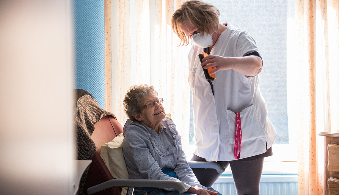 A nursing home aide holds a phone to assist a nursing home resid