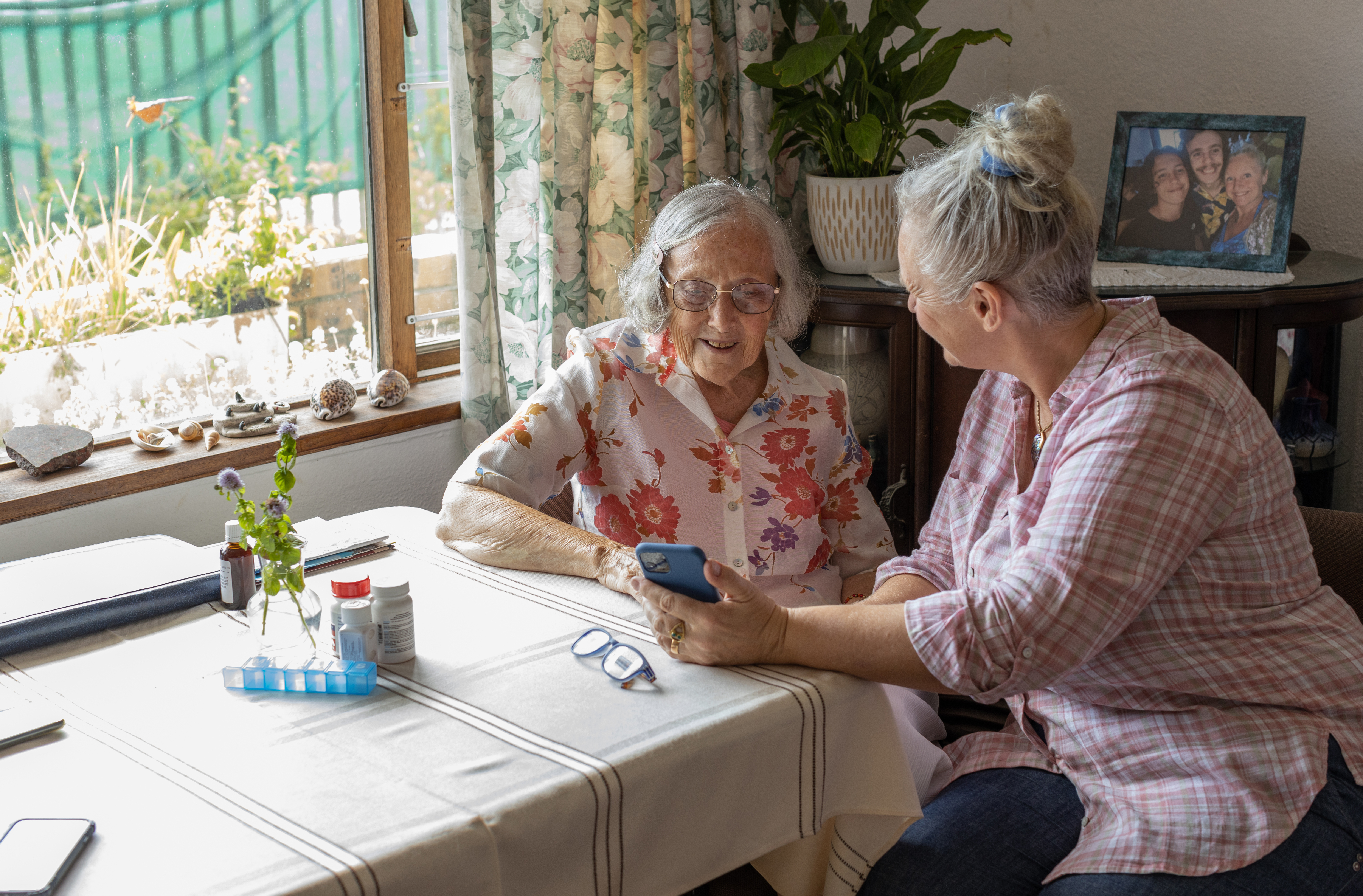 Mature female carer showing senior woman photos on a smart phone