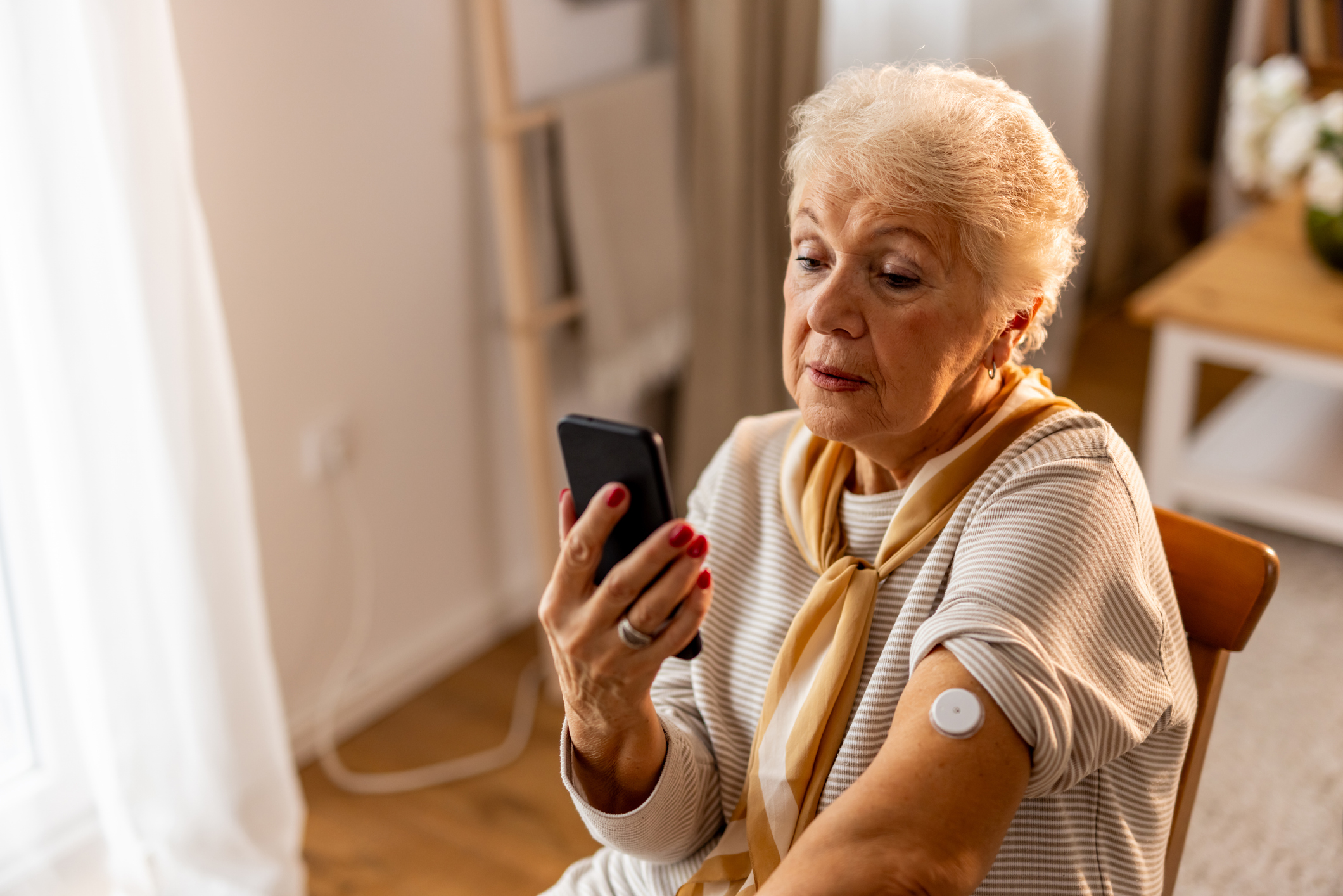 Senior woman checking sugar or glucose level by tapping mobile phone to sensor at home - concept of technology, diabetes and health care