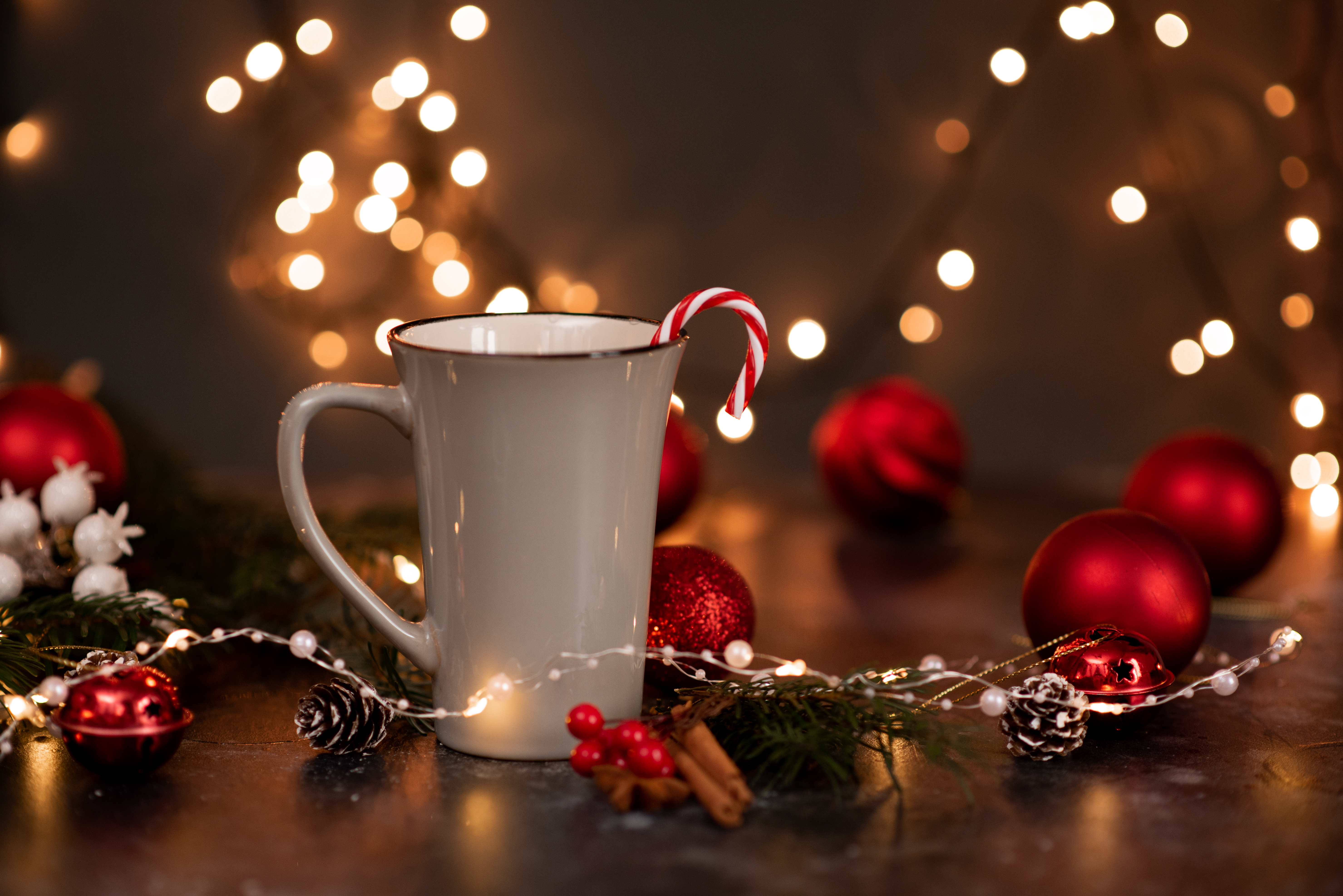 Enamel cup of hot cocoa with marshmallows and candy canes in the shape of a heart against rustic background with beautiful Christmas lights of bokeh. Could also be coffee. Blurred background.