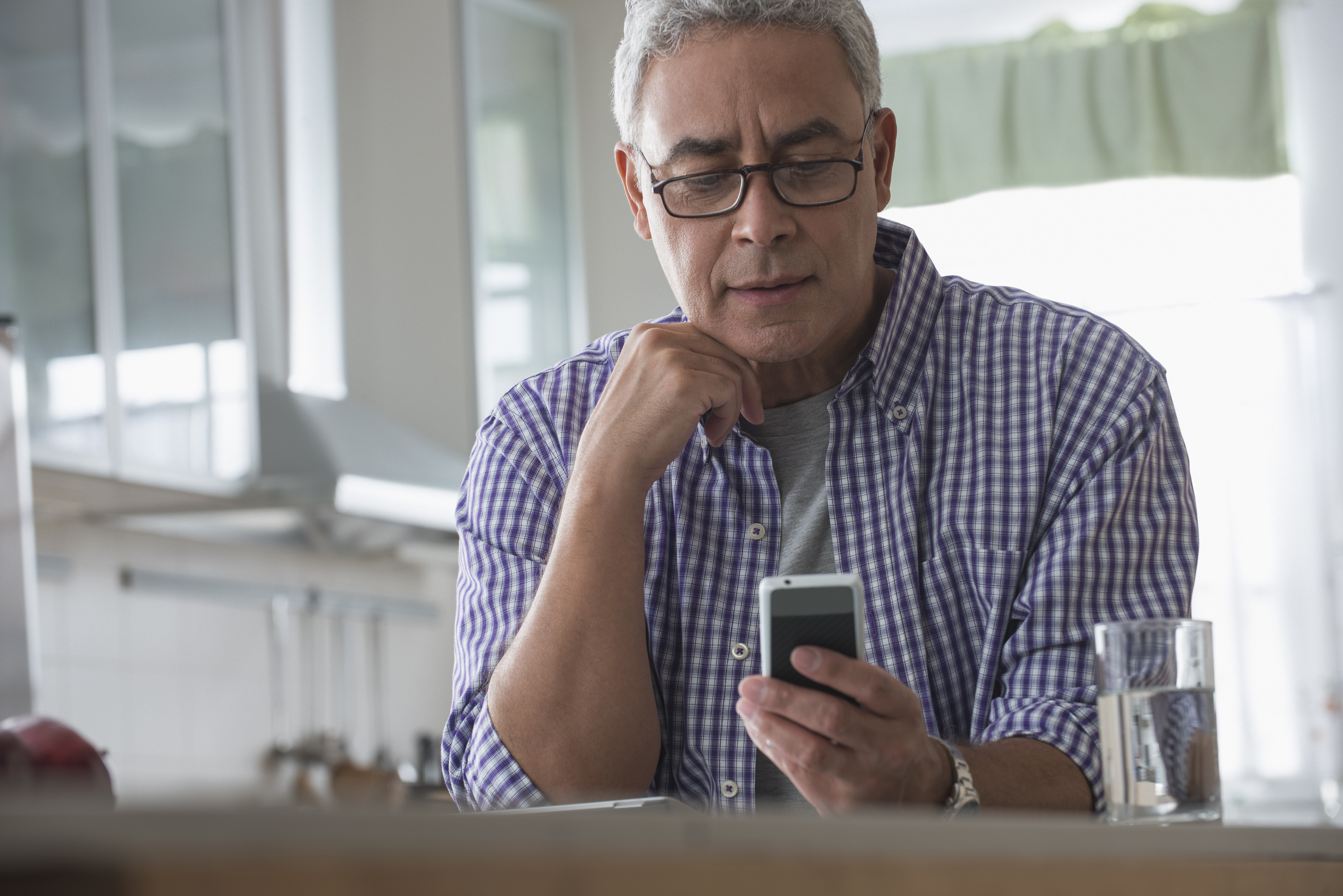 Hispanic man using cell phone in kitchen