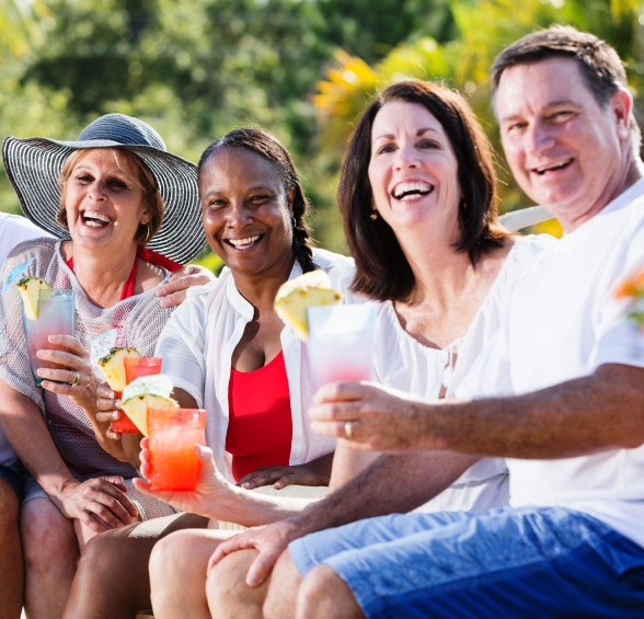 Multi-ethnic mature adults (50s, 60s) enjoying tropical drinks.  Main focus on African American woman in middle.