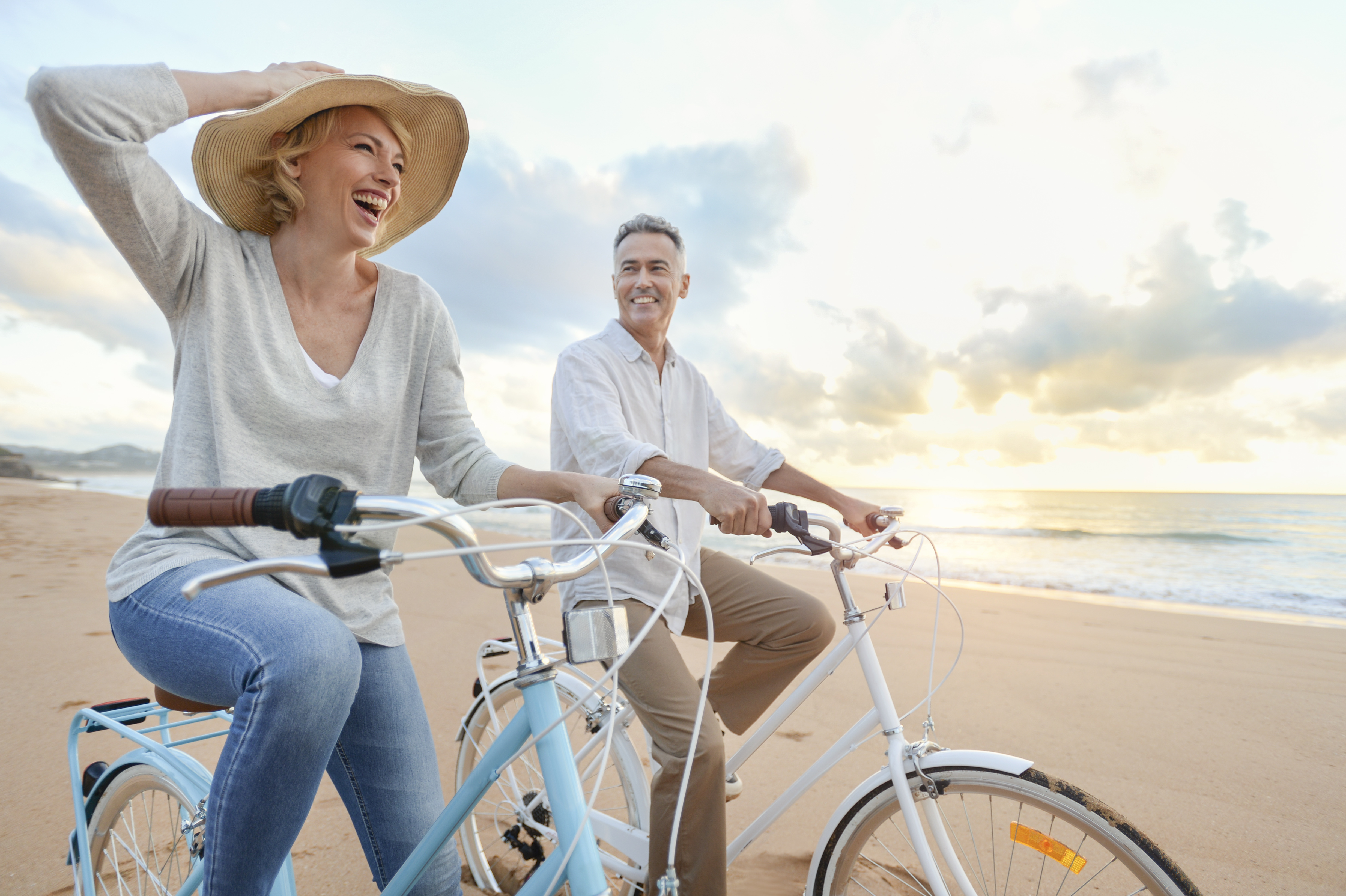 Mature couple cycling on the beach at sunset or sunrise.