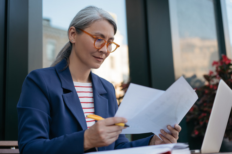 Mature businesswoman reading contract, planning project, brainstorming. Portrait of attractive asian secretary reading, working with documents, sitting at workplace