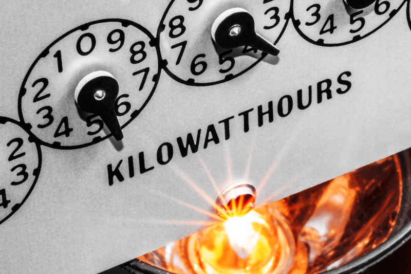 Kilowatt hour electric meter register dials with light bulb shining below