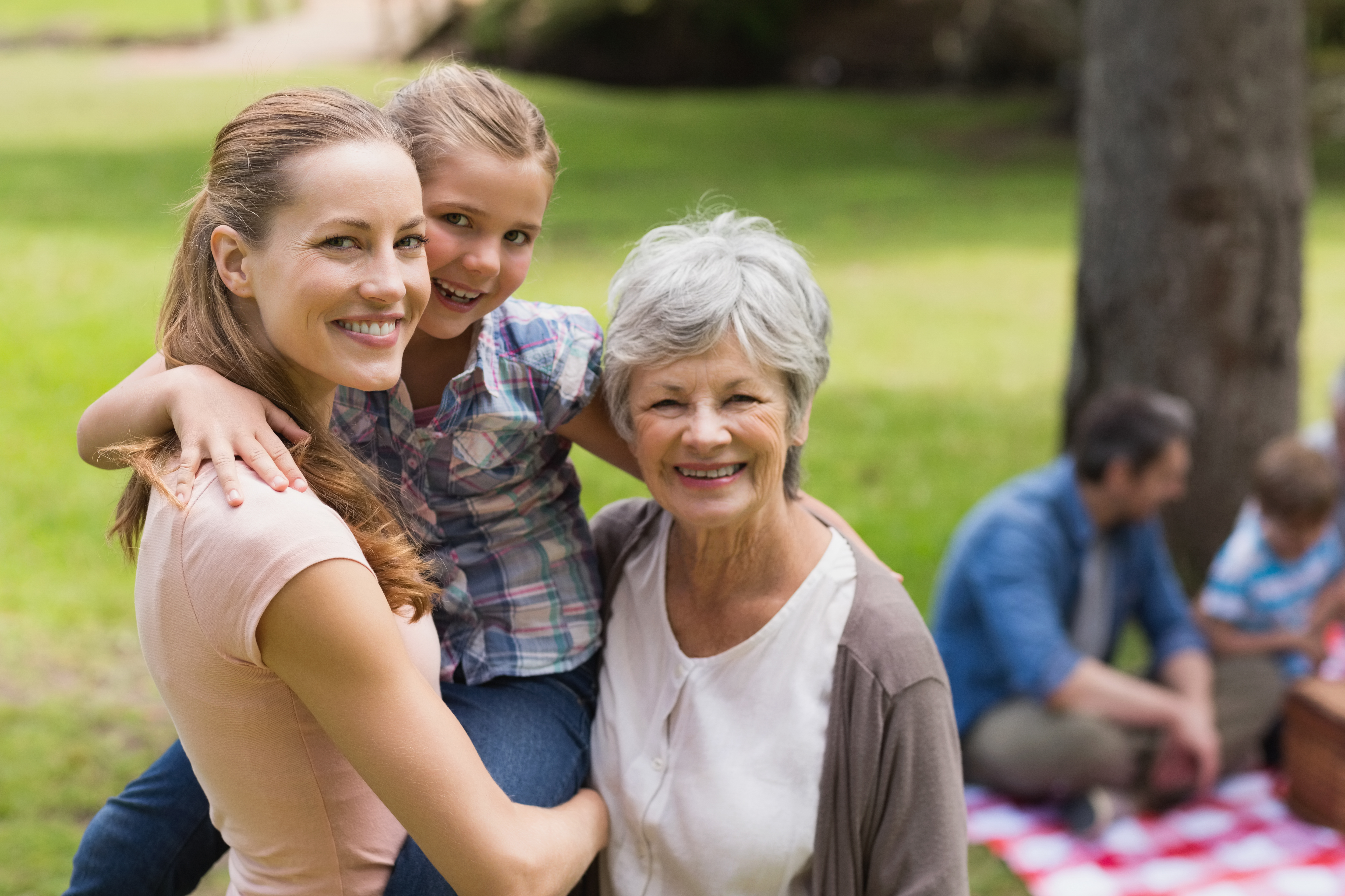 Grandmother mother and daughter with family in background at park