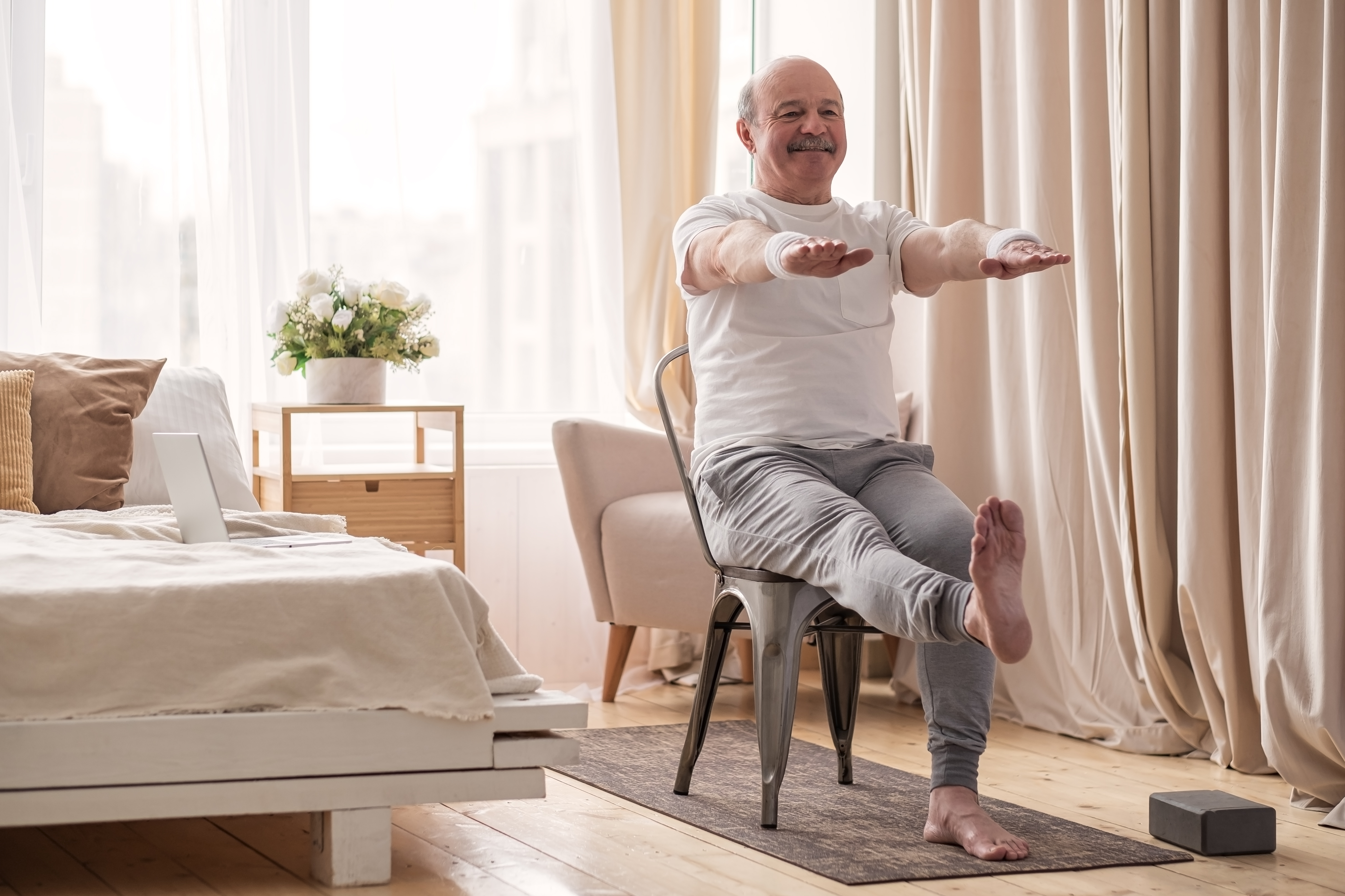 Elderly man practicing yoga asana or sport exercise for legs and hands on chair