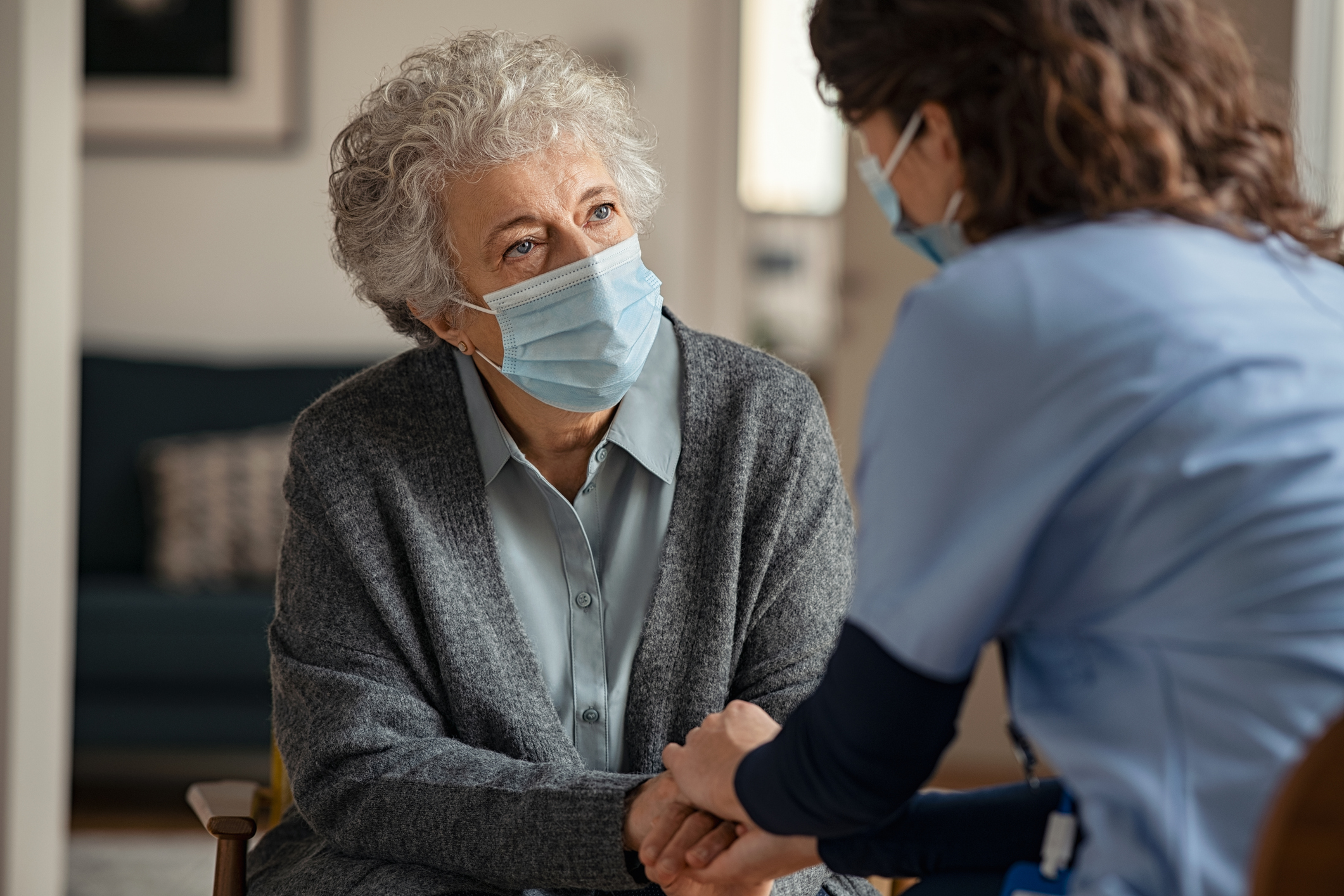 Female doctor consoling senior woman wearing face mask during home visit