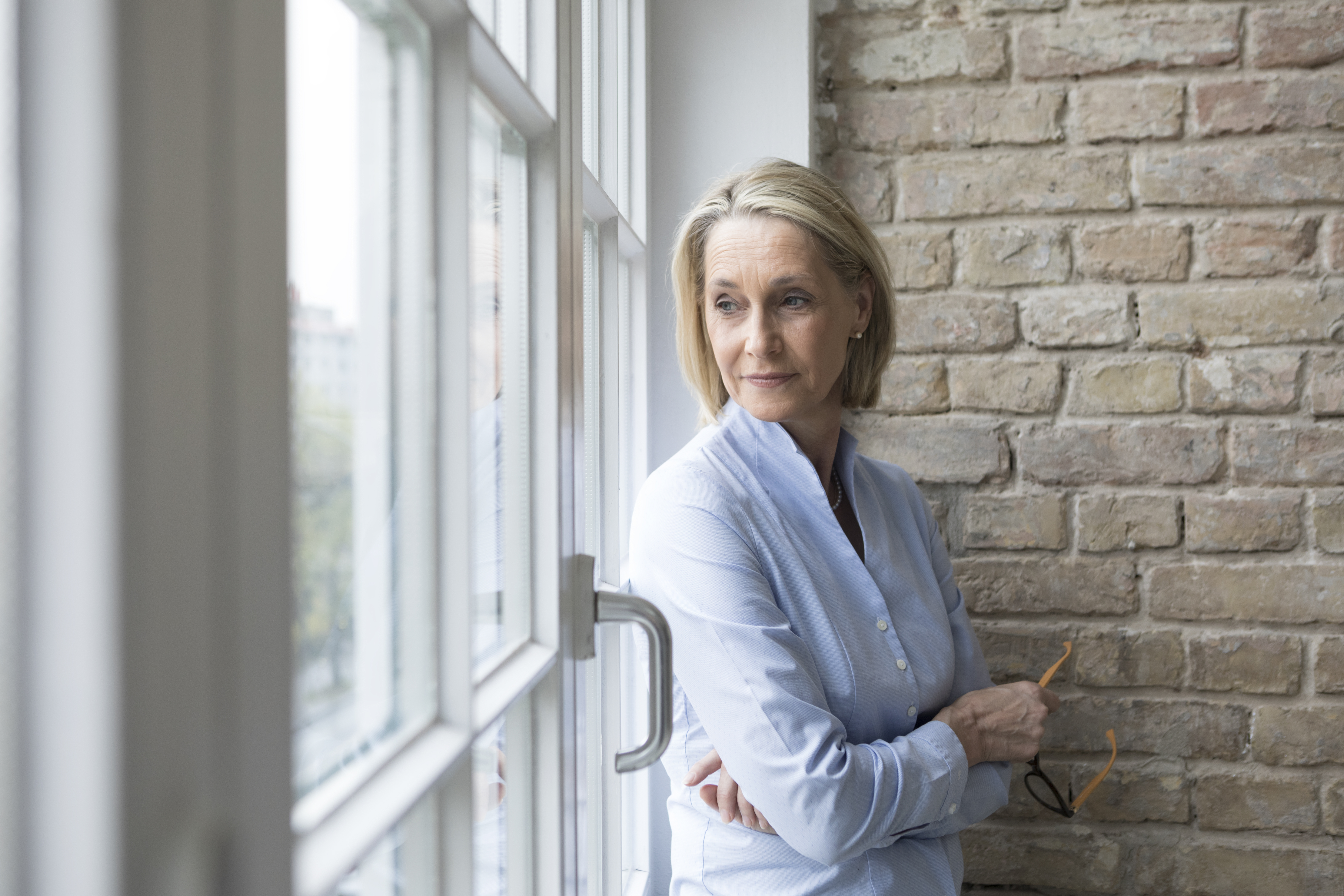 Mature businesswoman standing at window, looking worried